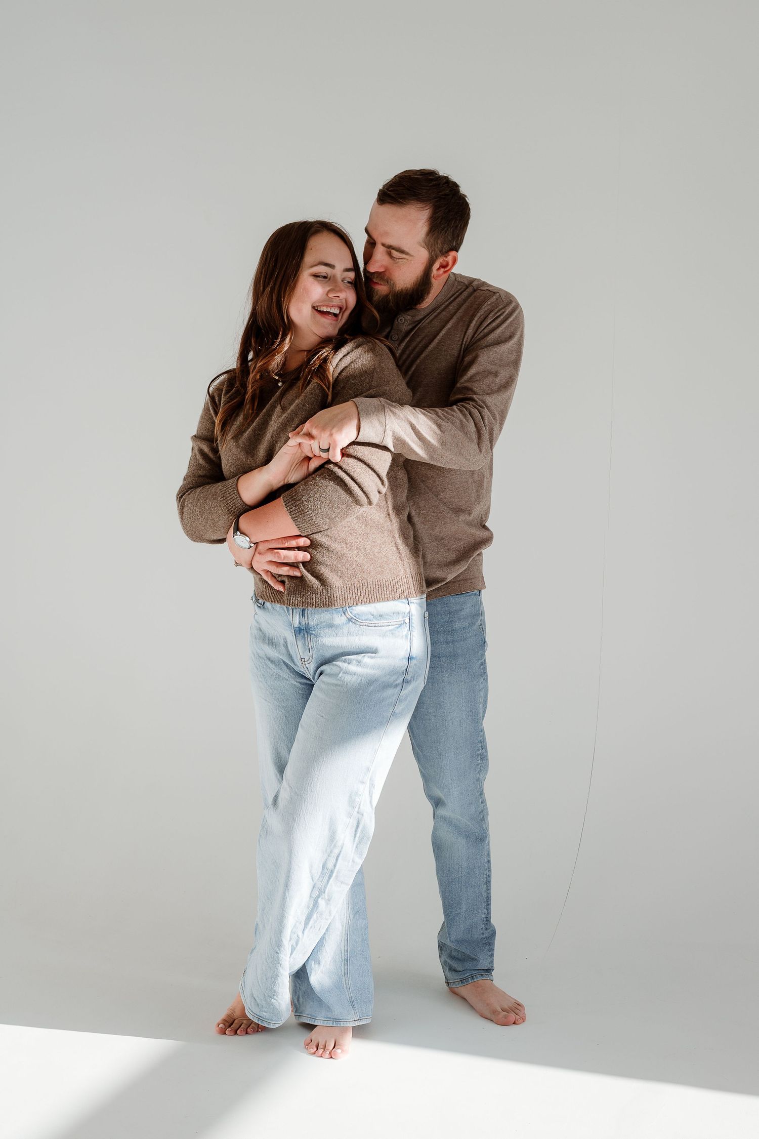 A couple in casual attire embraces and laughs together against a white backdrop in a series of candid photos.