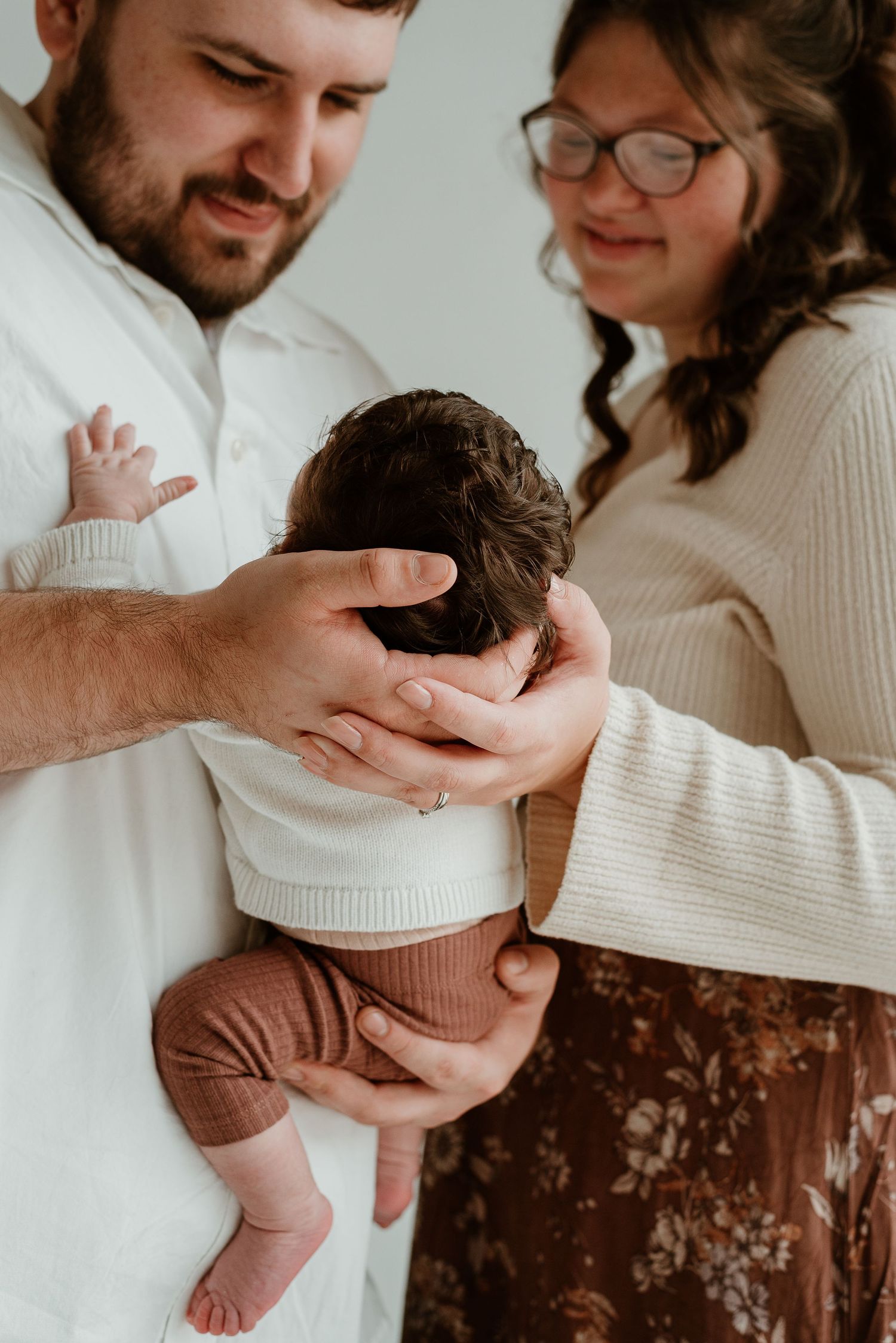 Parents in white sweaters lovingly hold and gaze at their newborn baby in a series of tender moments.