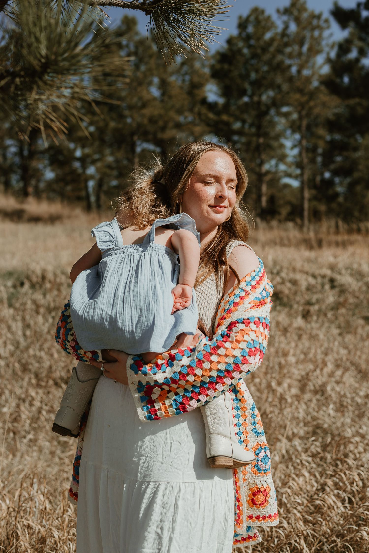 An intimate outdoor portrait featuring a light blue dress and colorful crocheted cardigan.