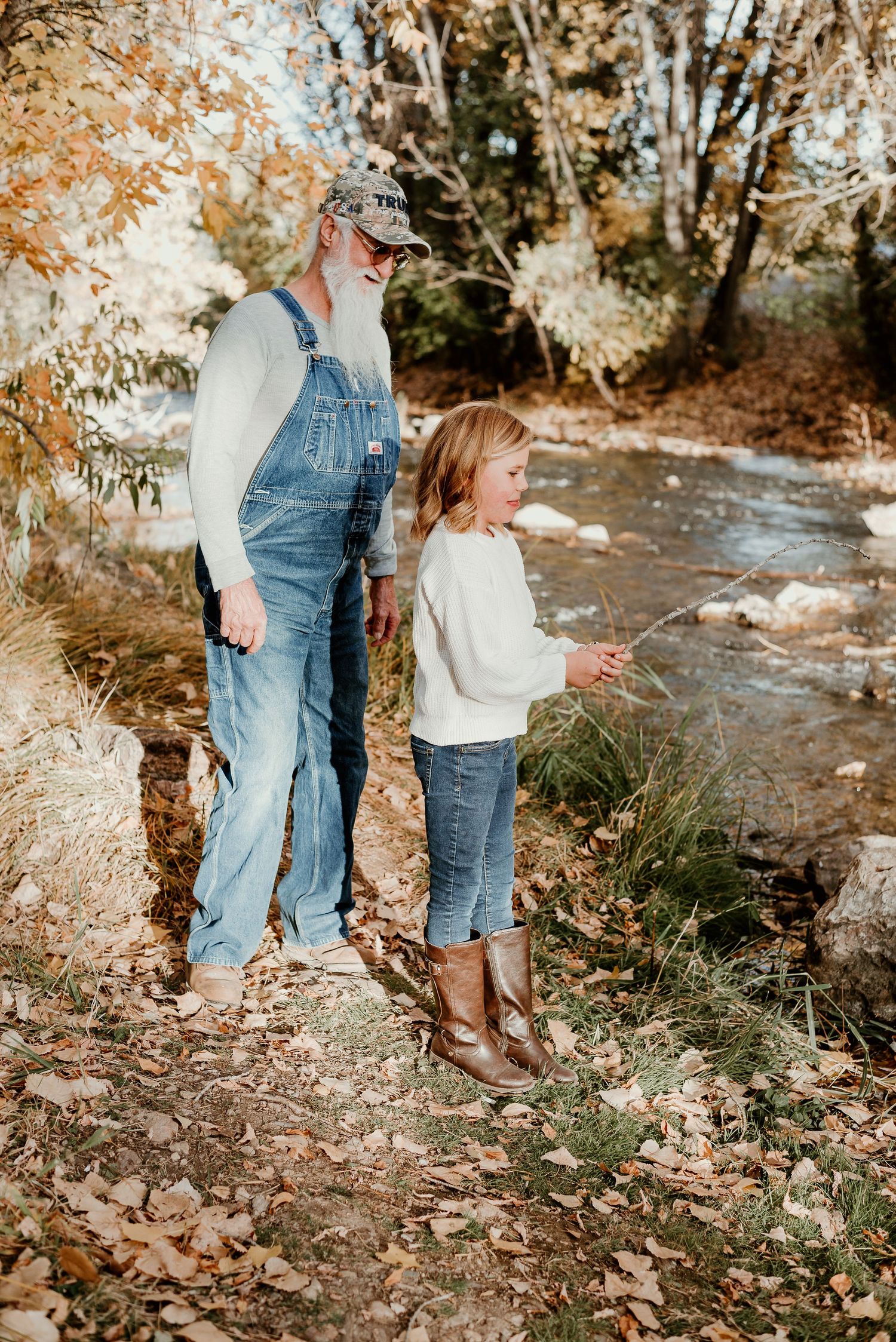 Family members standing by a stream in autumn with fallen leaves on the ground.