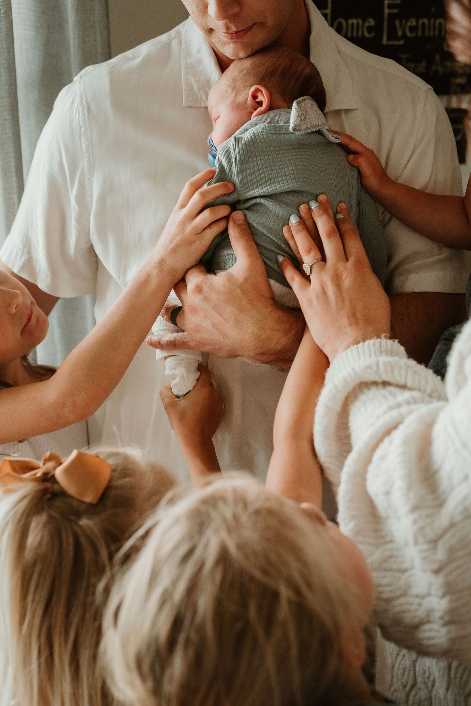 Close-up shots of hands reaching to touch and hold a small baby in sage green clothing.