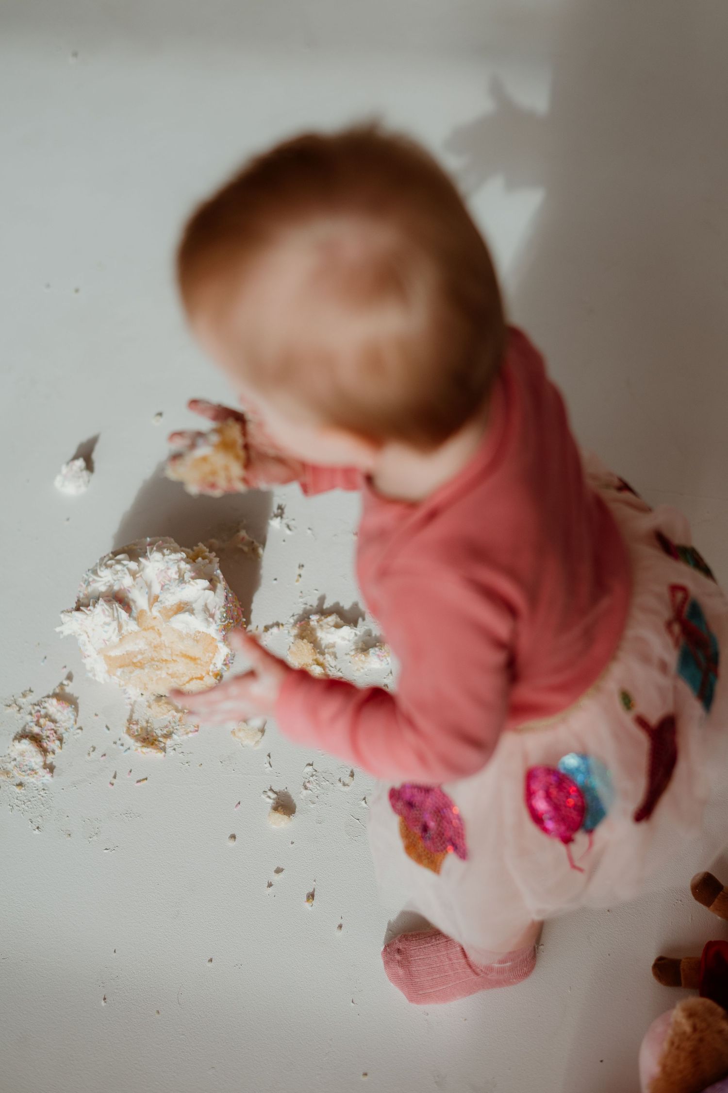 Baby in pink sweater smashes and plays with cake during messy first birthday cake smash photo session.