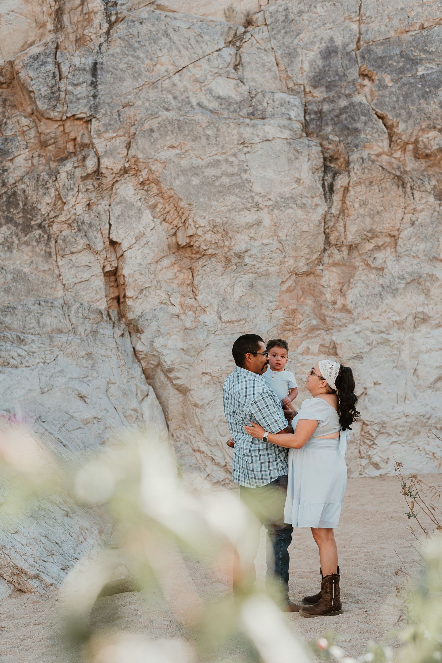 A couple shares an intimate moment against a textured rock wall backdrop in soft natural lighting.