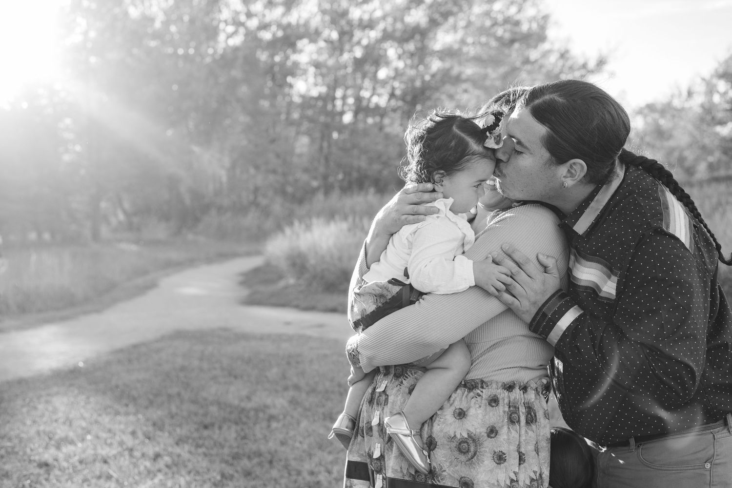 A tender outdoor family moment captured in black and white during golden hour on a rural path.