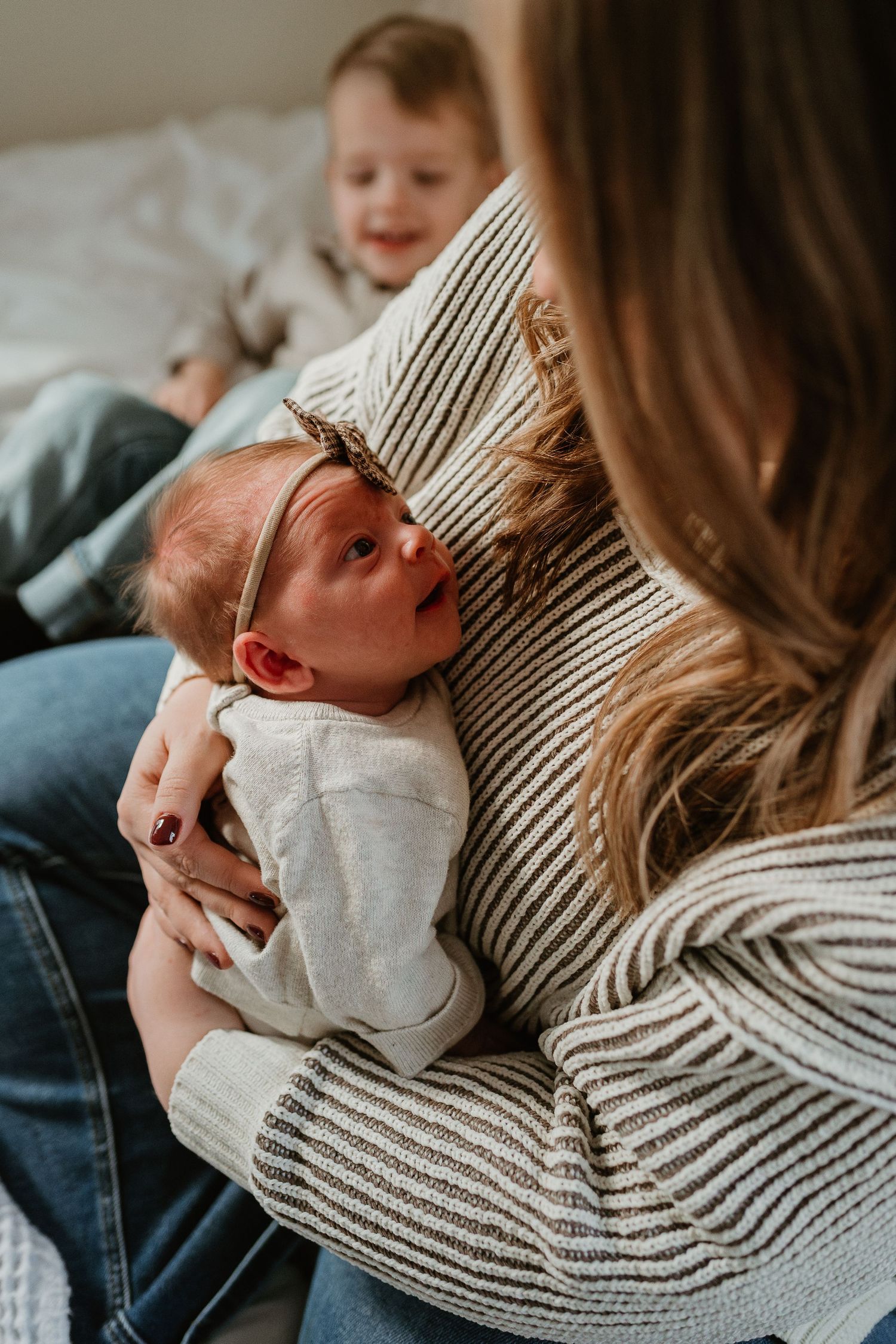 Newborn baby in white onesie being cradled against person wearing striped sweater.