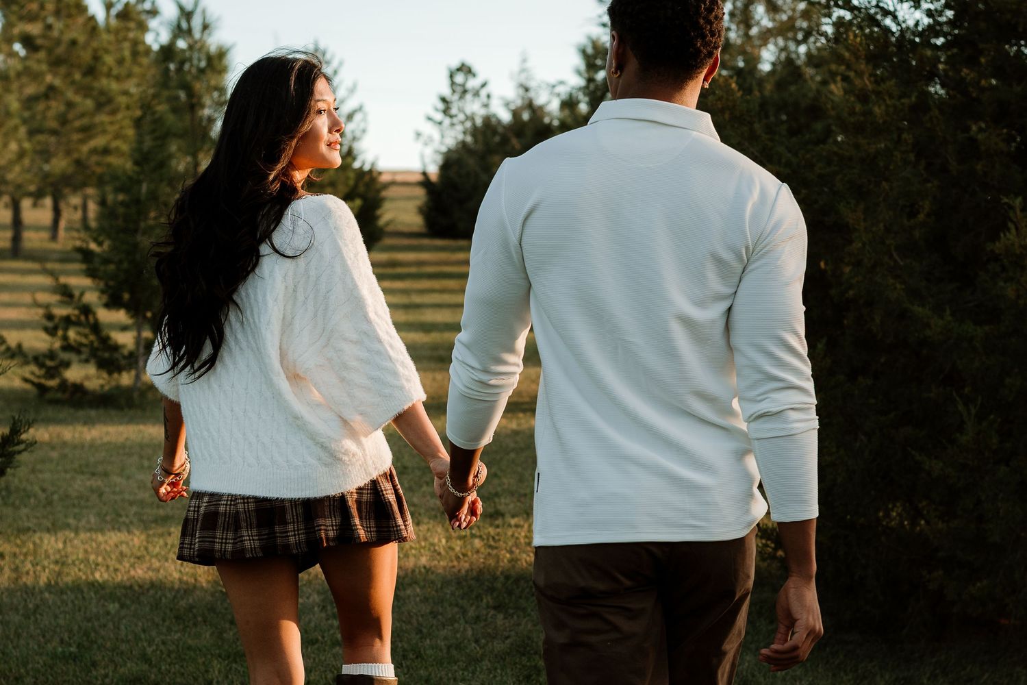 Couple walking hand in hand through a sunlit outdoor setting wearing coordinated outfits.