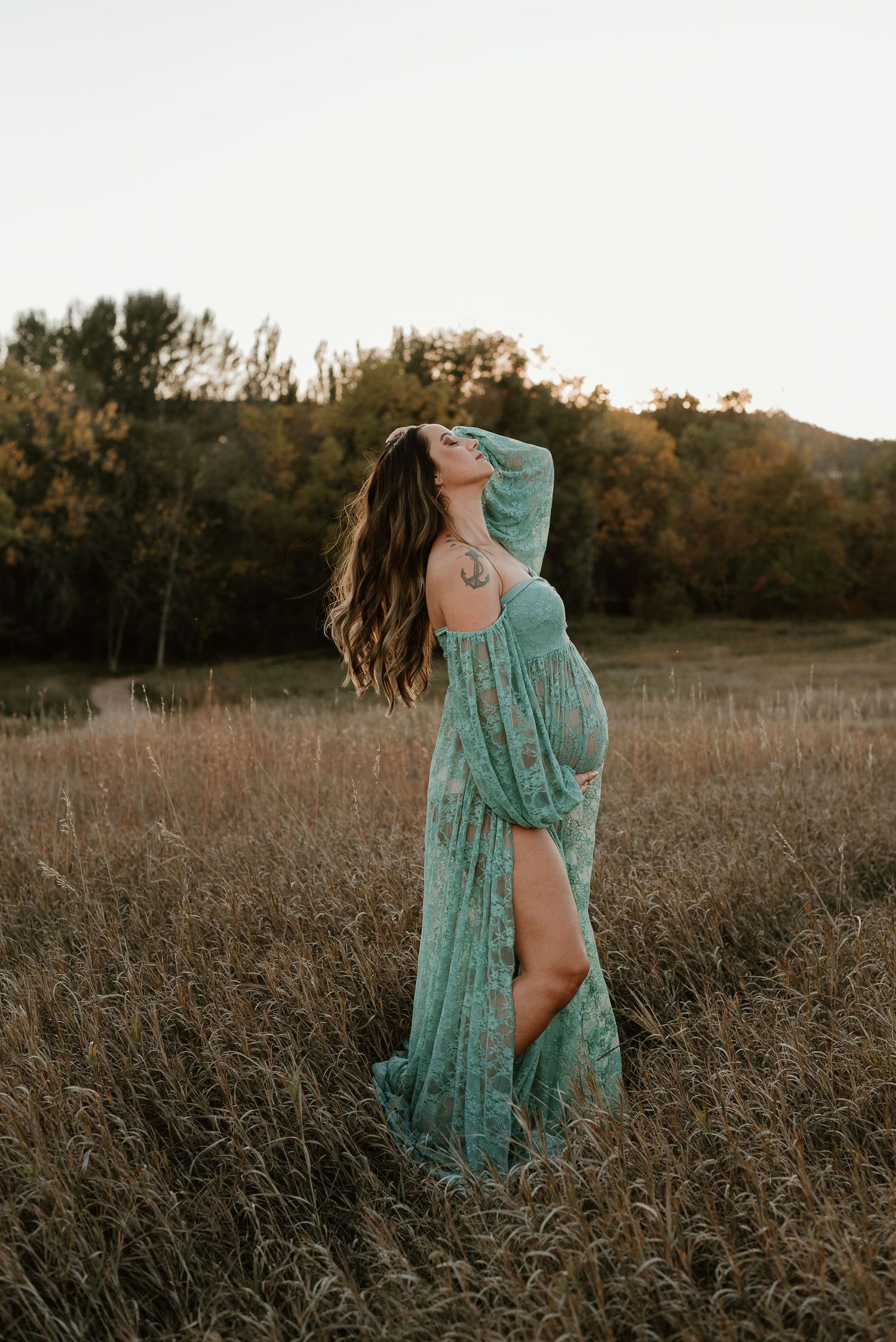 A figure in a flowing turquoise dress poses gracefully in a golden field at sunset.