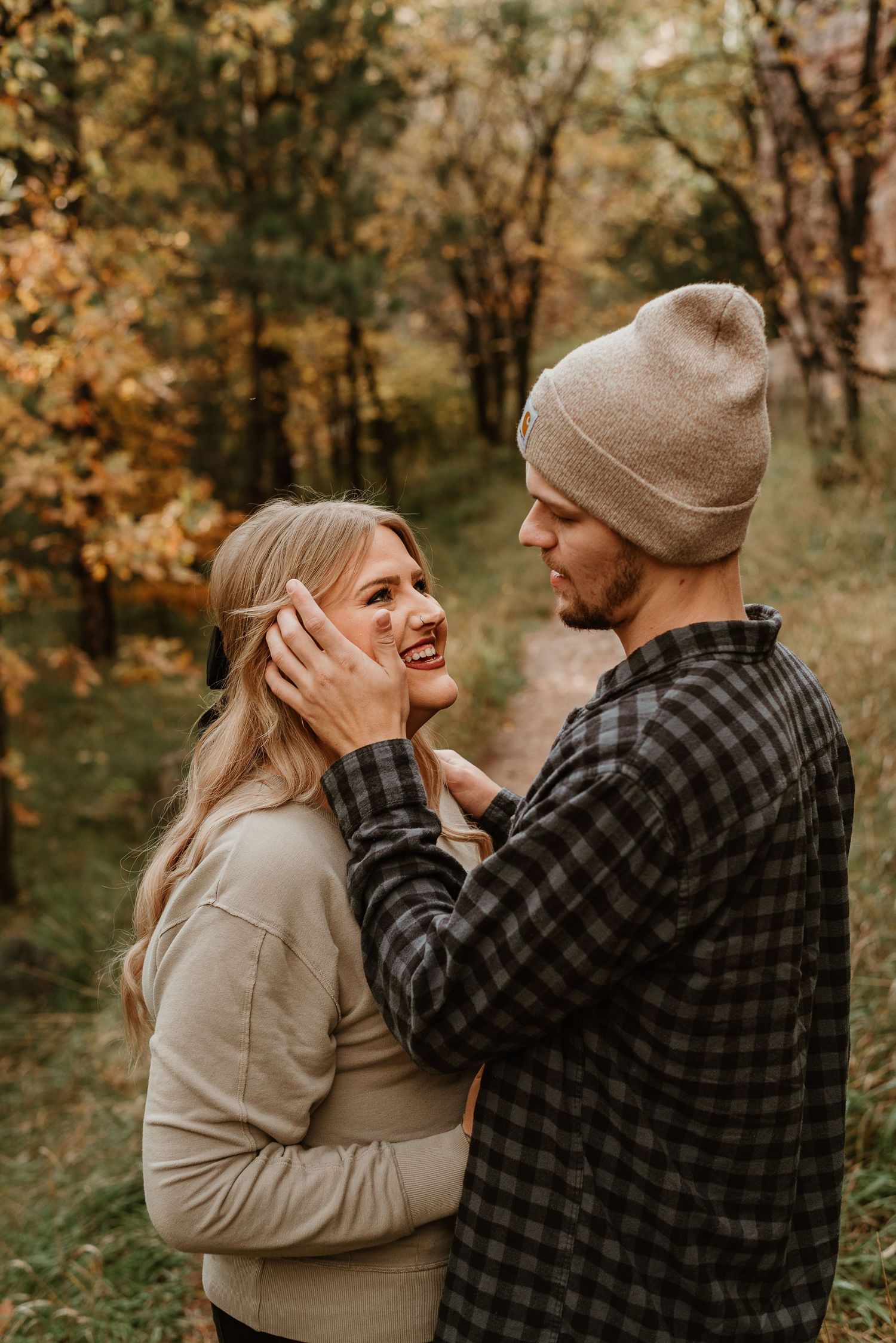 A couple shares tender moments in autumn woods wearing casual attire and embracing each other lovingly.