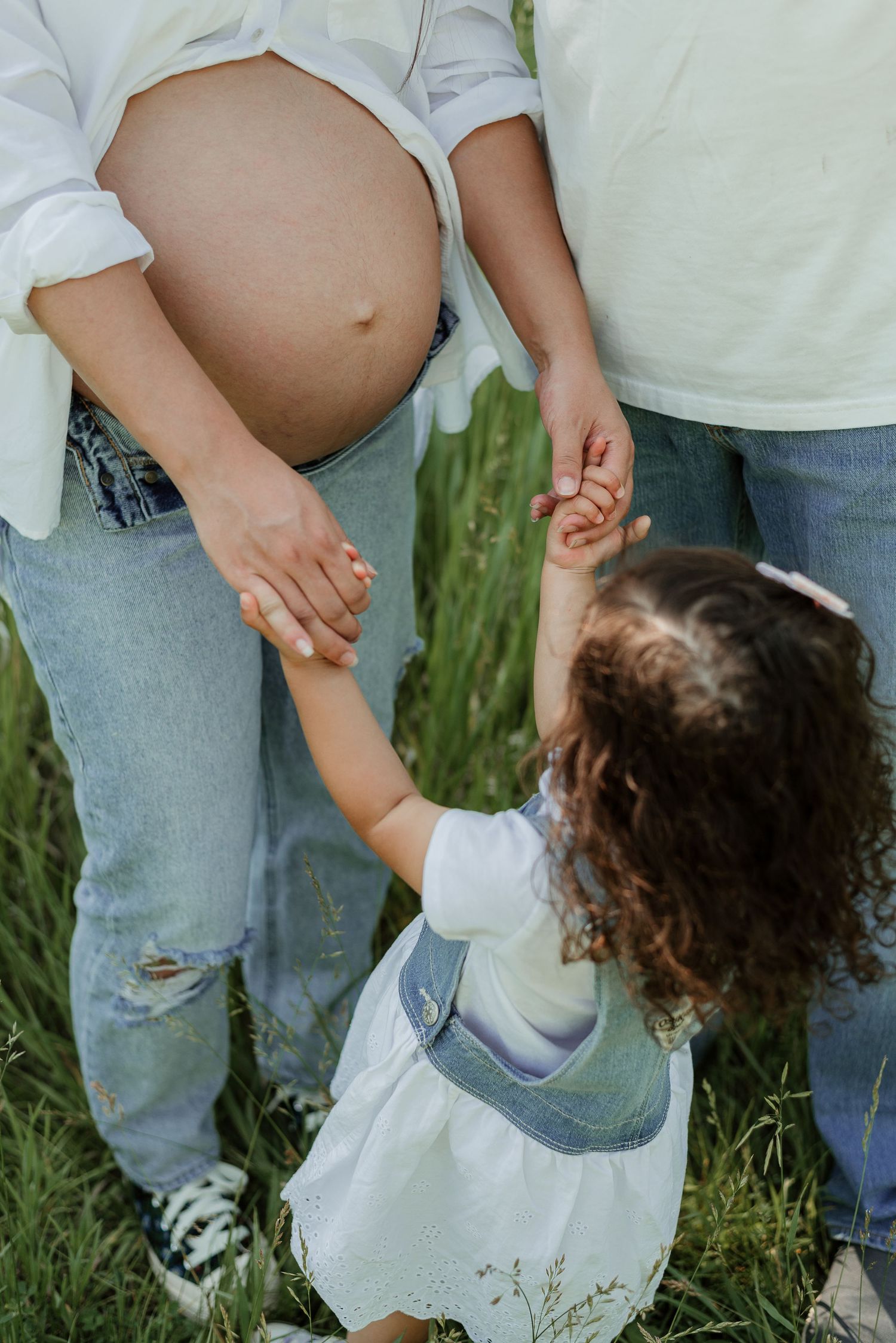 A small child reaches up to touch a pregnant belly in an outdoor setting.