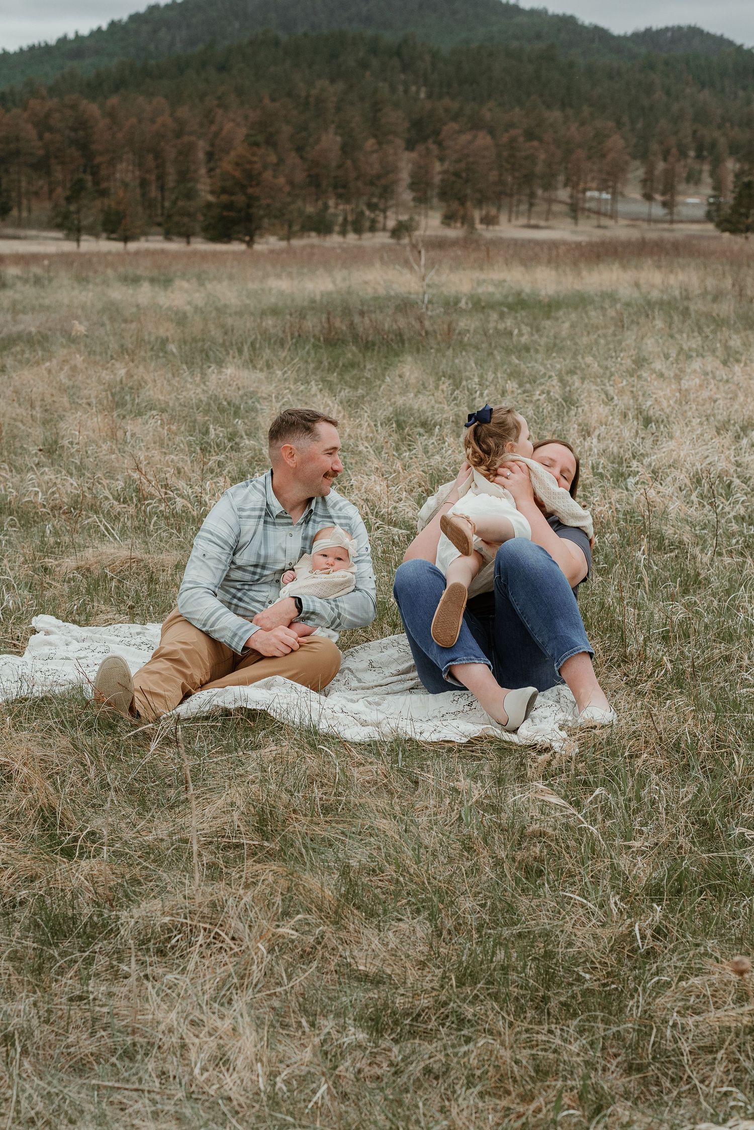 Family lying together on a blanket in a scenic mountain meadow.