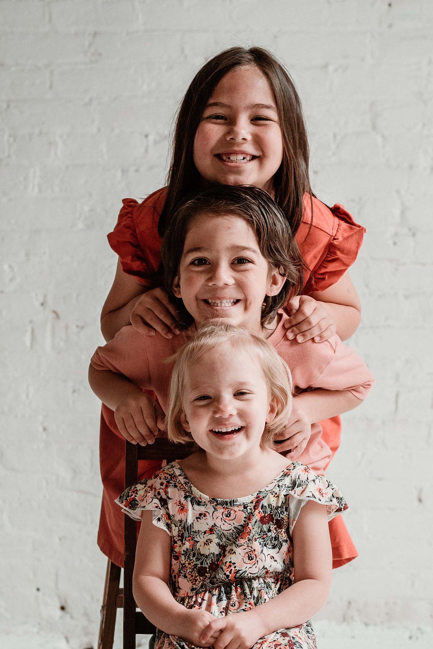 Three children pose playfully stacked together against white background.