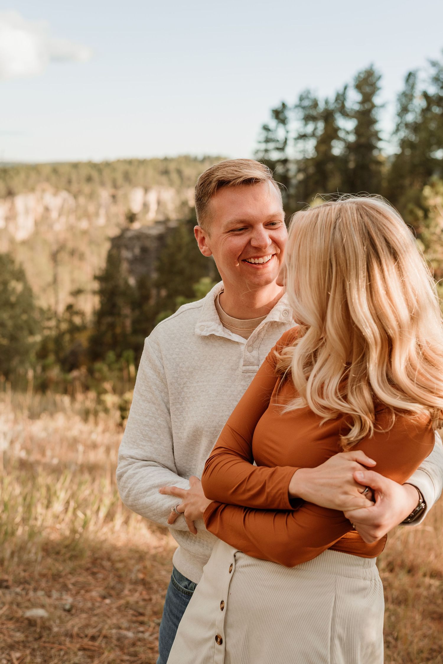 Couple embracing and laughing during autumn outdoor photoshoot in cream and rust colored outfits.