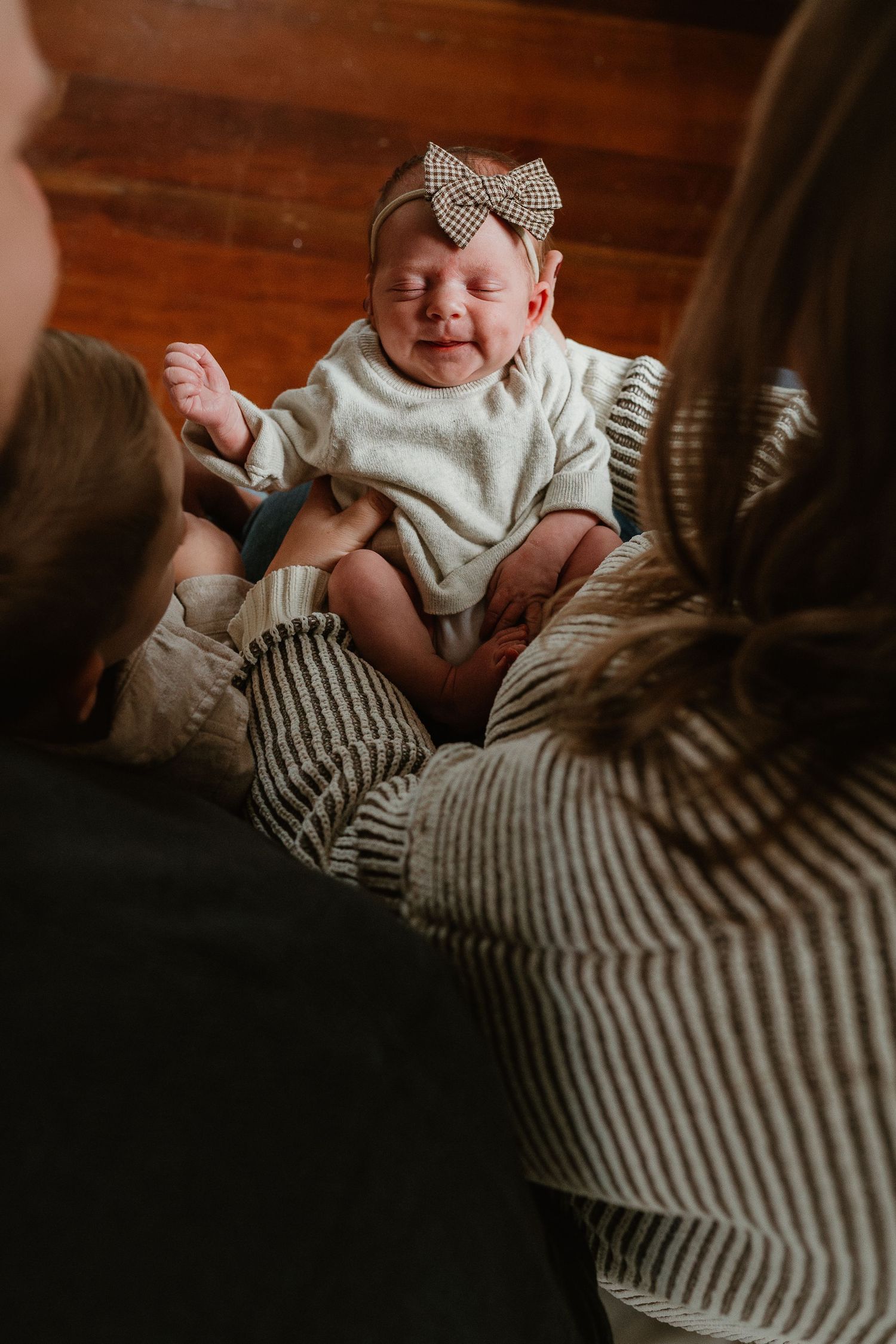A baby wearing a white outfit and bow headband rests against a striped sweater.