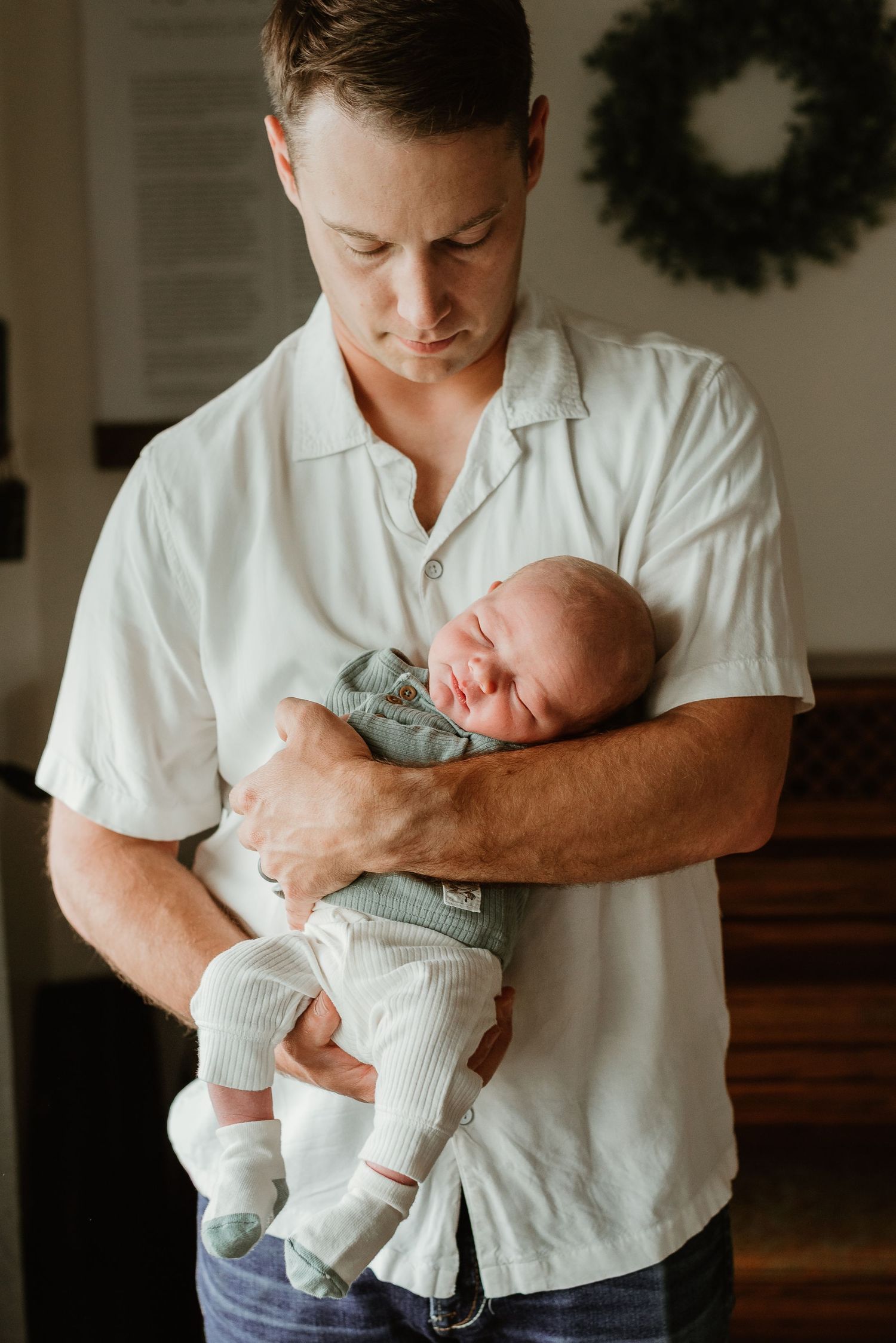 Parent in white shirt holding and gazing at newborn baby dressed in light colored outfit.