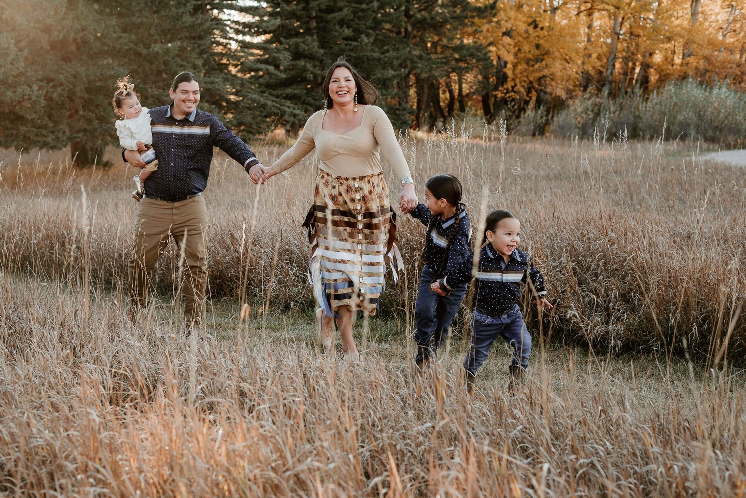 Family members playing and running through autumn field with evergreens in background.