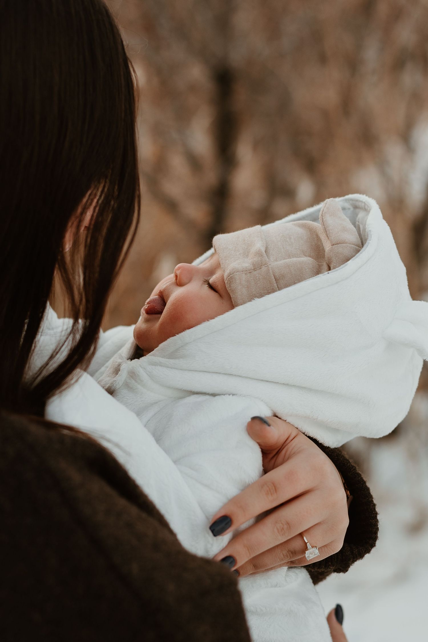 Close-up of a sleeping newborn baby wrapped in white blankets being held with dark painted nails visible.