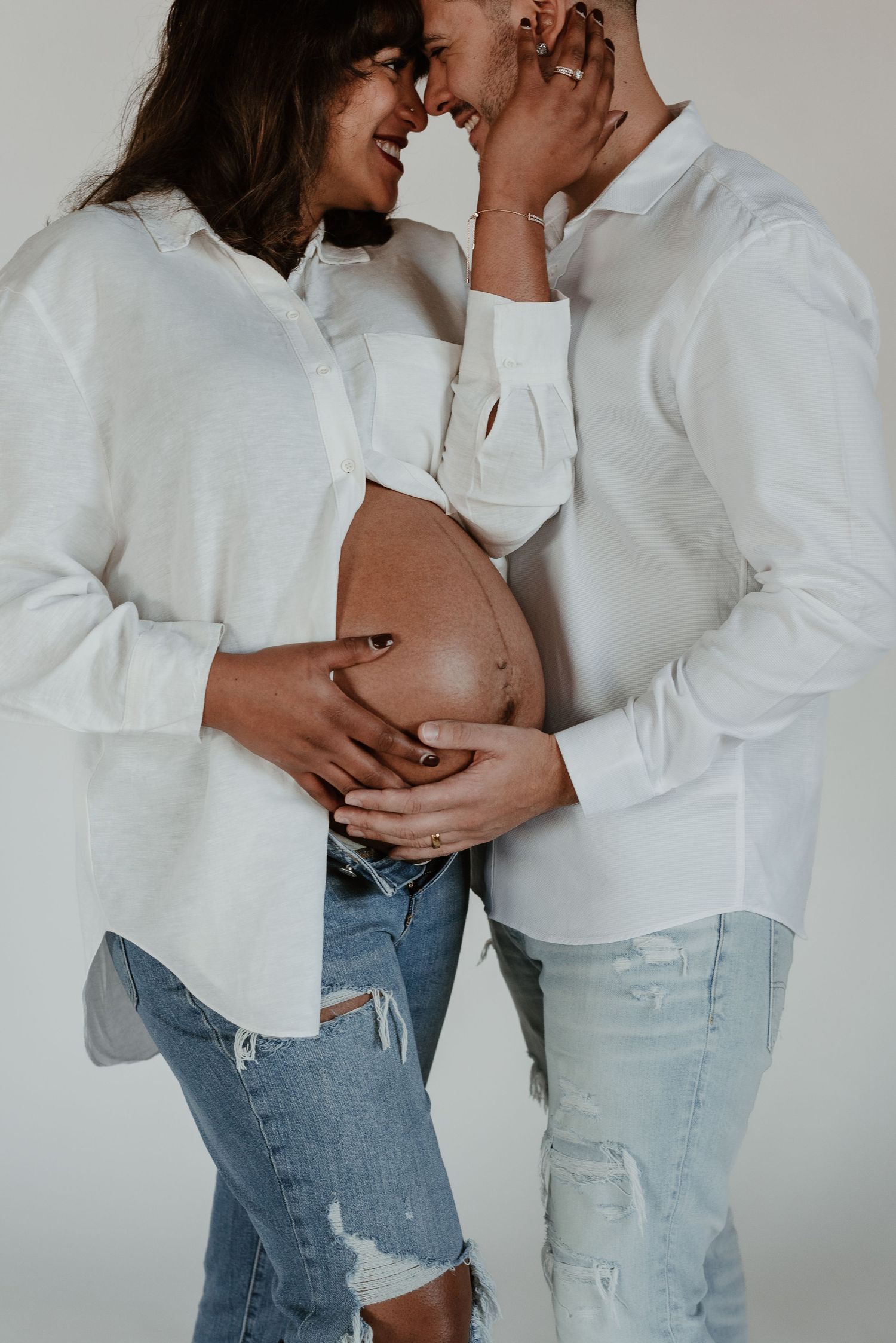 Romantic maternity photo with couple in white shirts sharing intimate moment.