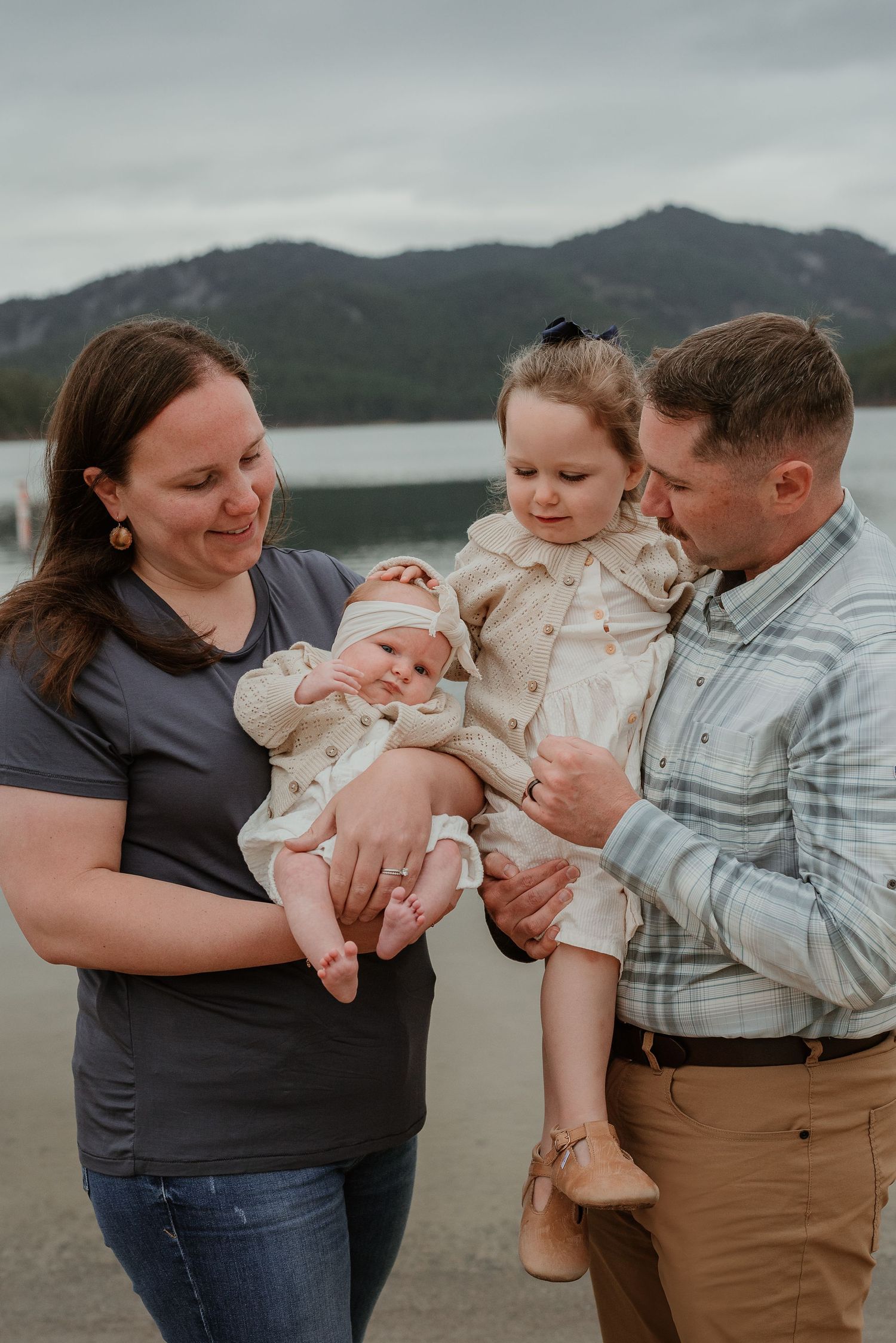 A family shares a tender moment outdoors with their baby against a mountain backdrop.