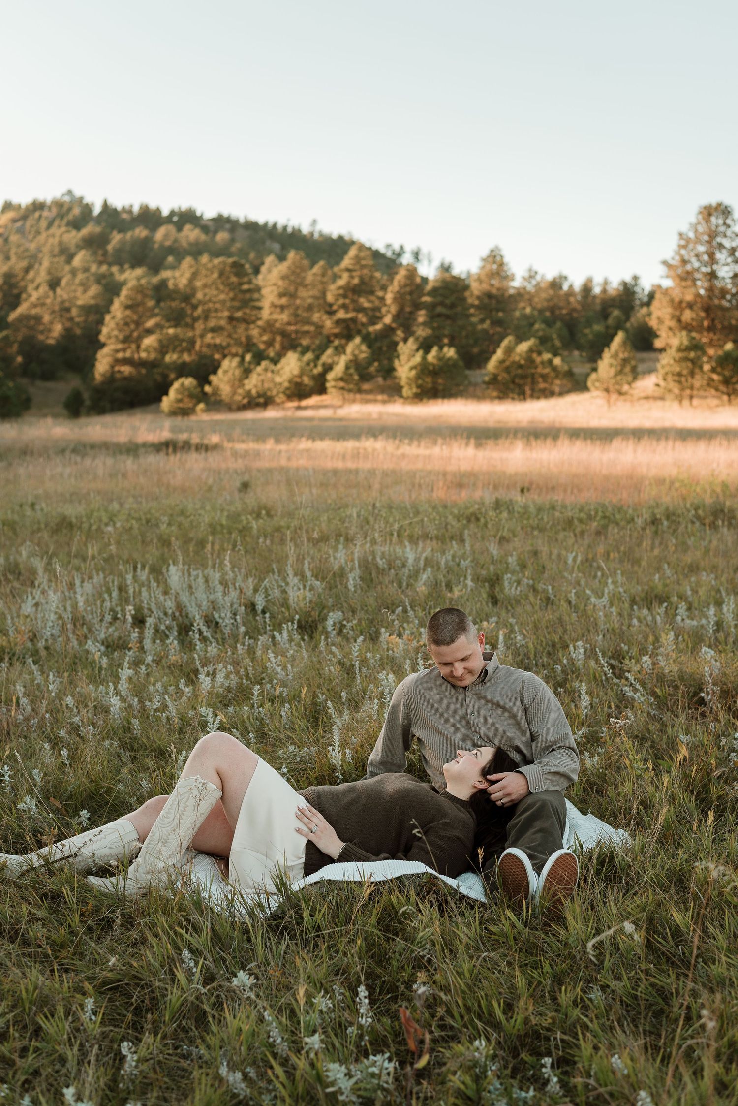 Couple relaxing in tall grass field during golden hour with forest in background.