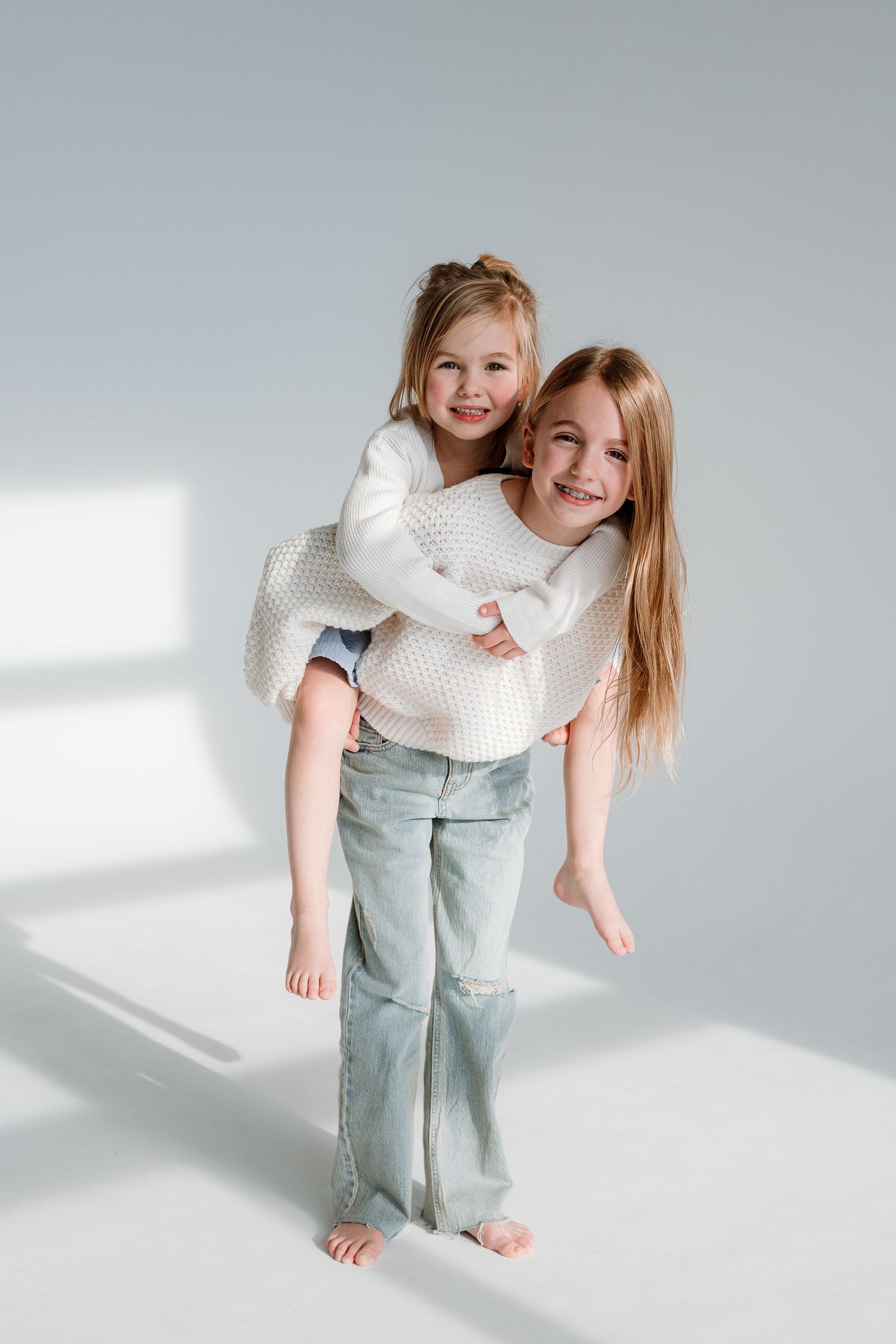 Child in white knit sweater and mint pants plays expressively in bright studio setting with natural light.