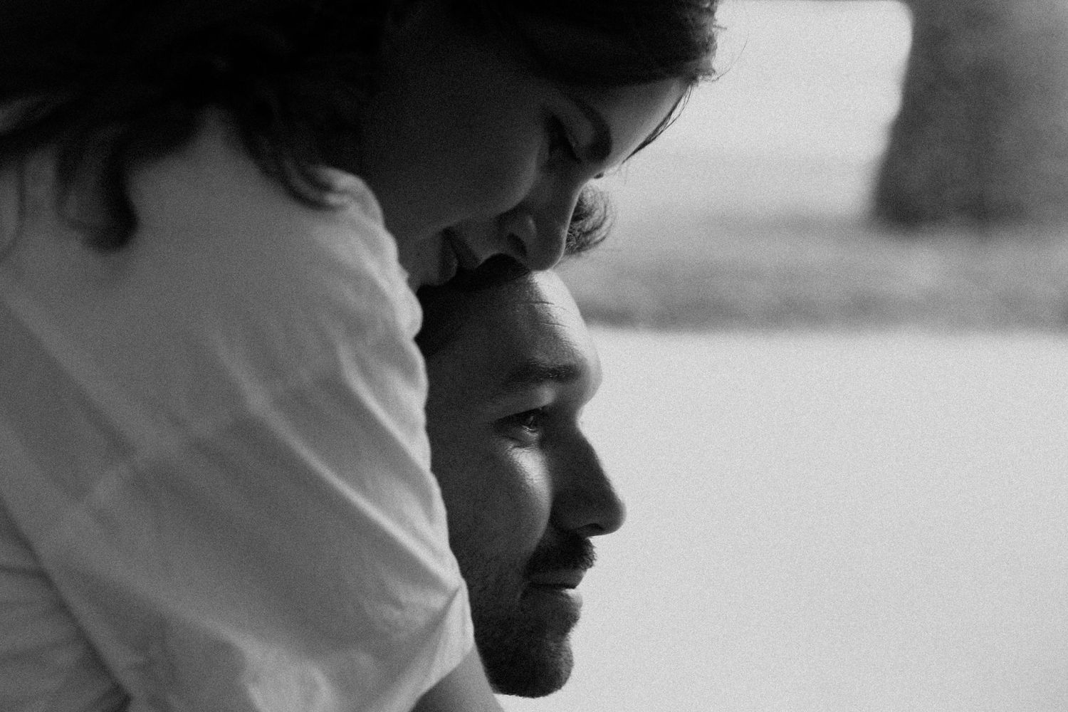 Black and white photo of a couple sharing an intimate moment, woman resting her head on a smiling mans shoulder.