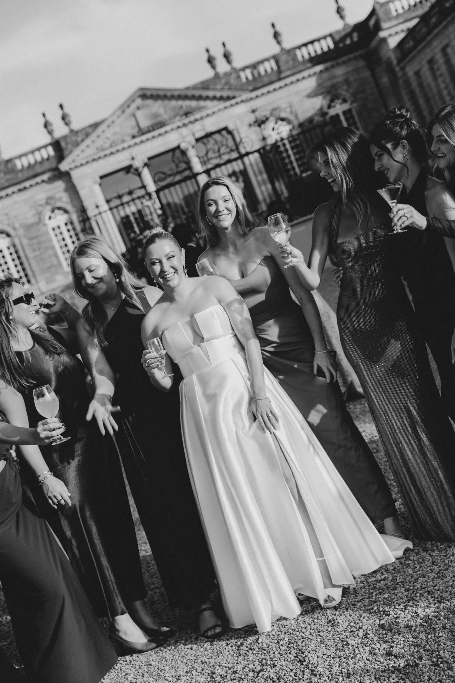 Black and white wedding photos showing a group of people in formal attire posing together on the grounds of a historic building.