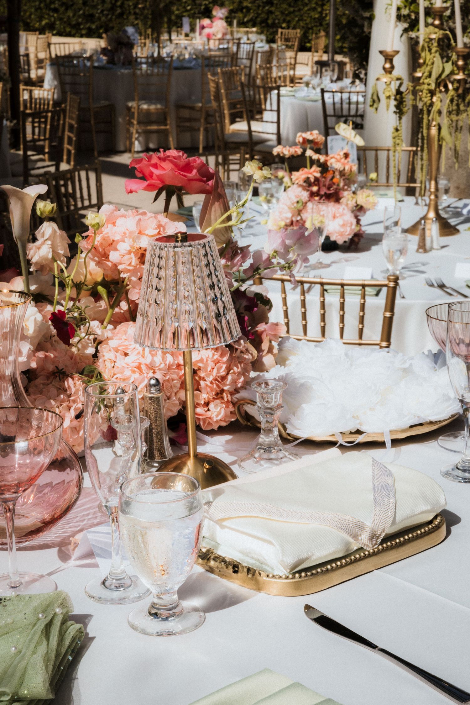 Elegant table settings with pink floral centerpieces, crystal glassware, and gold accents at a formal event.