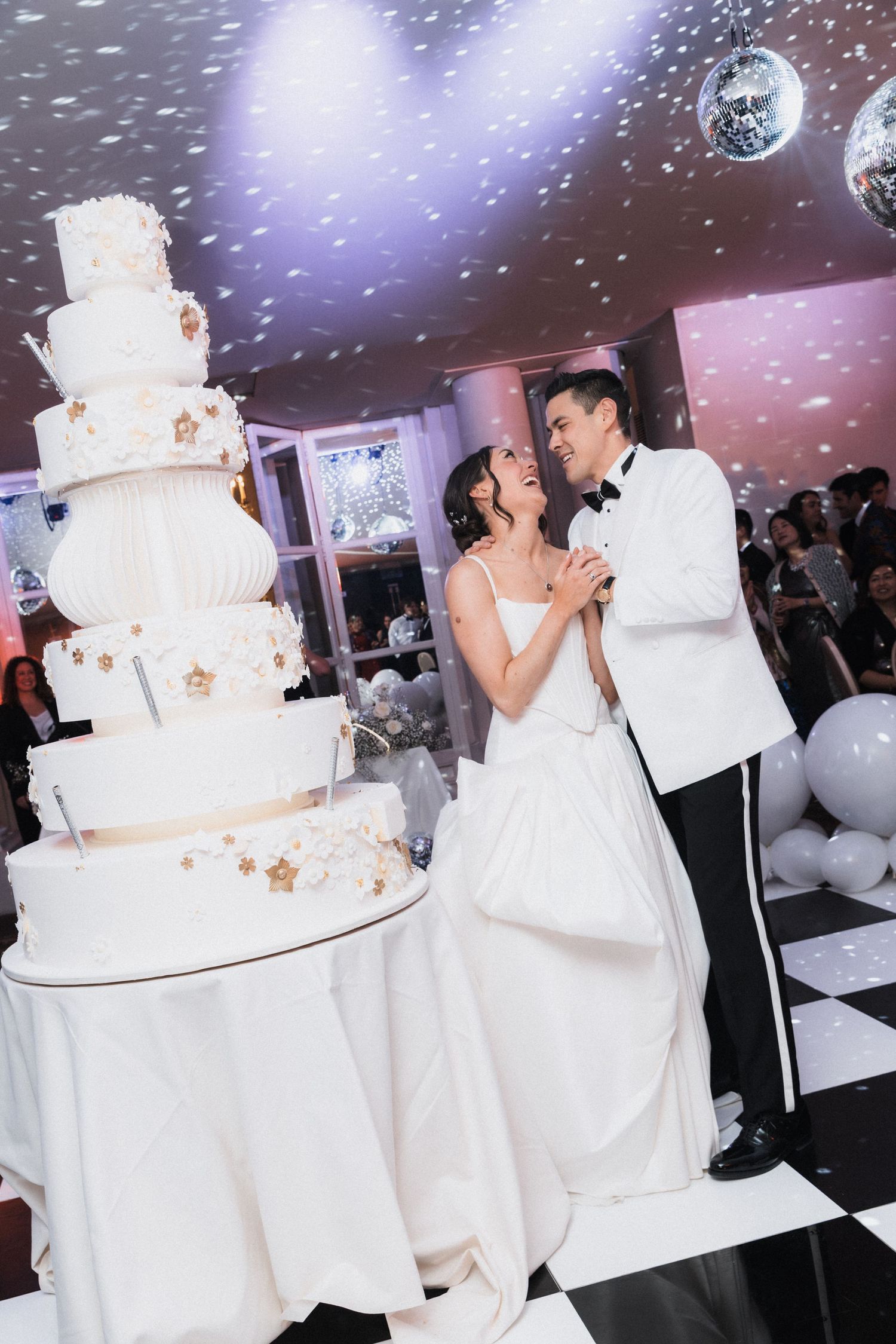 Elegant white wedding cake display with sparkling disco ball lighting effects.