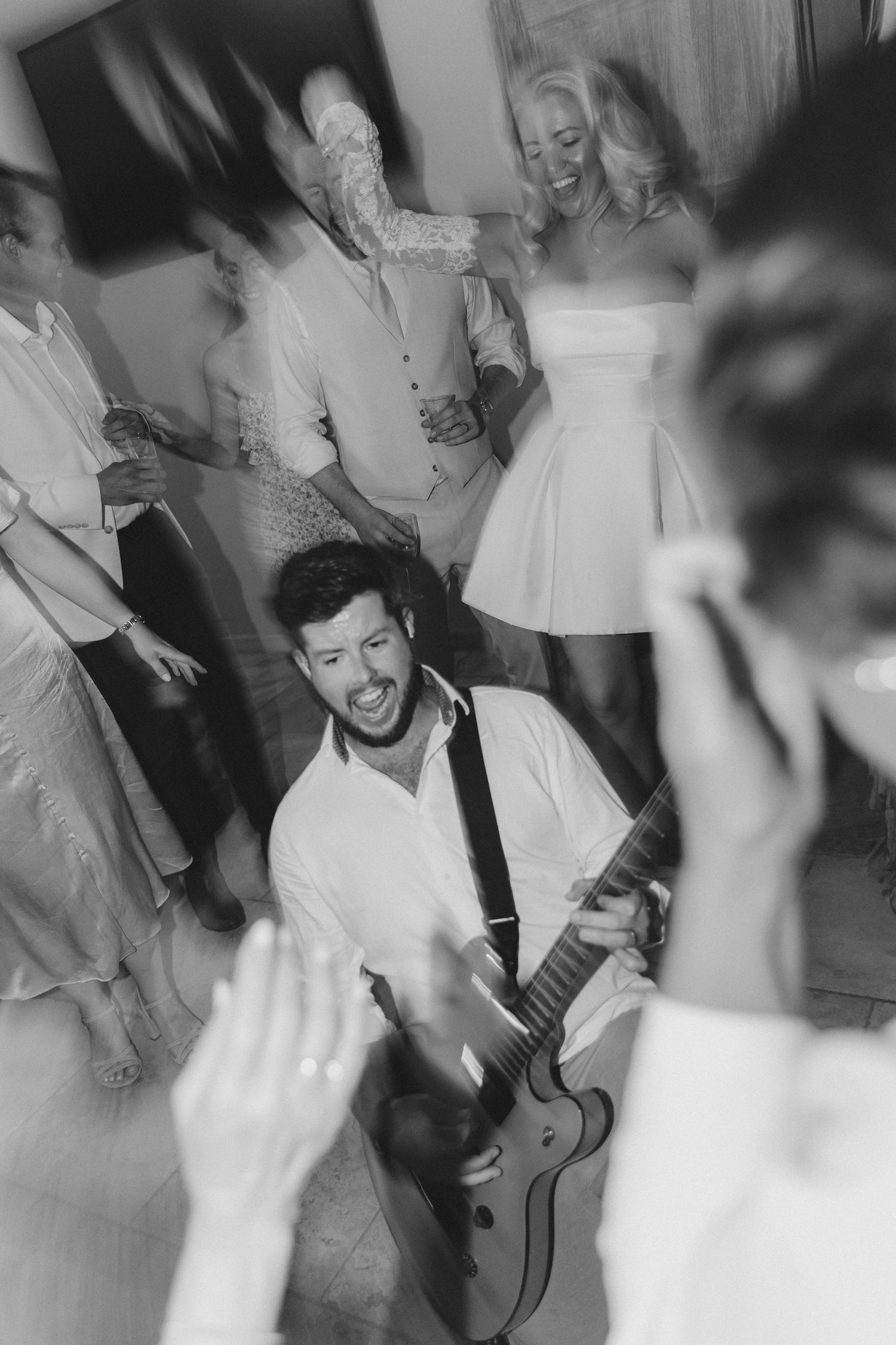 Wedding reception guests dance and celebrate with live music in a joyful black and white scene.