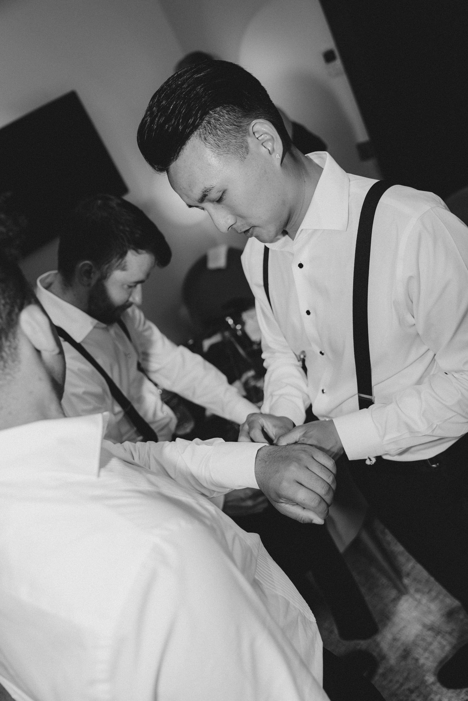 A person in formal attire with suspenders writes in a notebook in black and white.