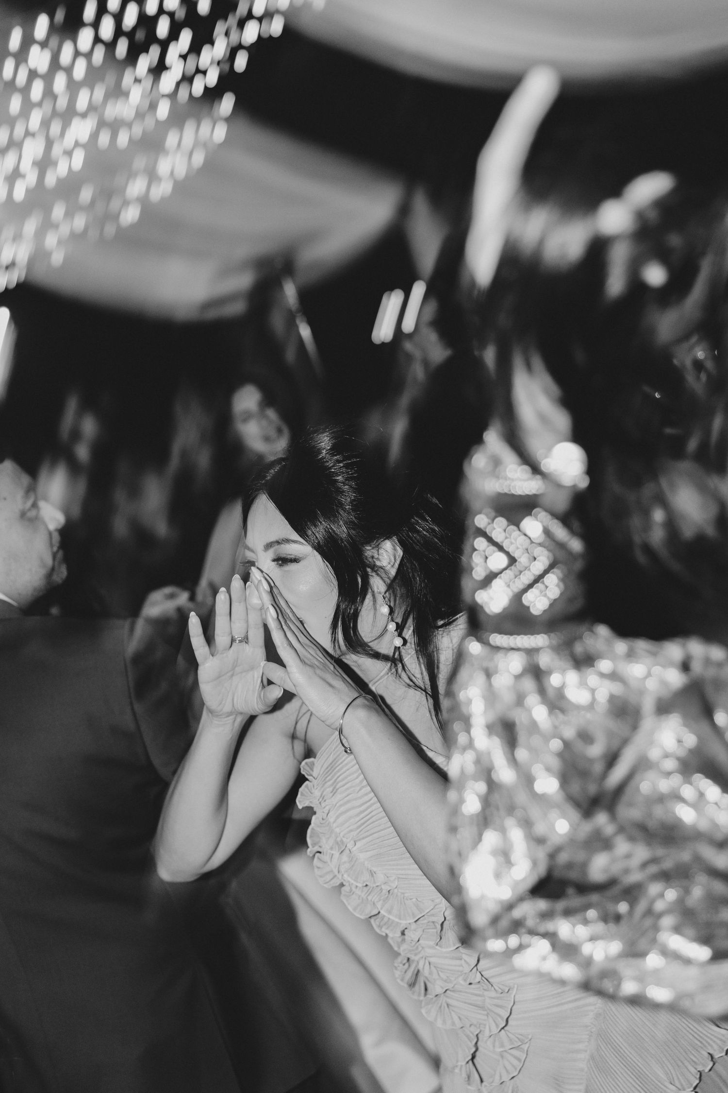 Black and white photo of guests dancing energetically at a lively wedding reception under string lights.