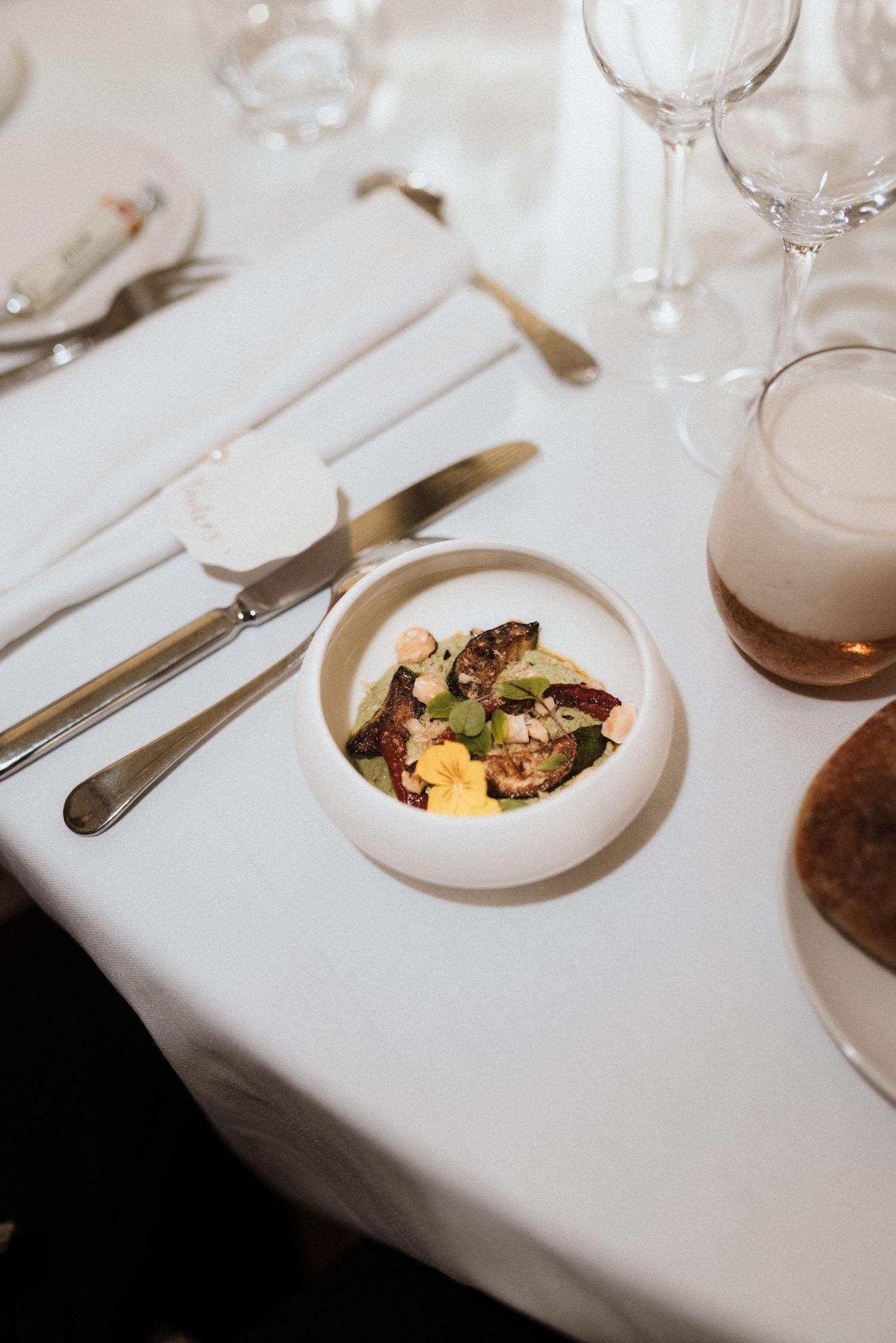White table setting at upscale restaurant with elegant wine glasses and plated dishes in soft lighting.