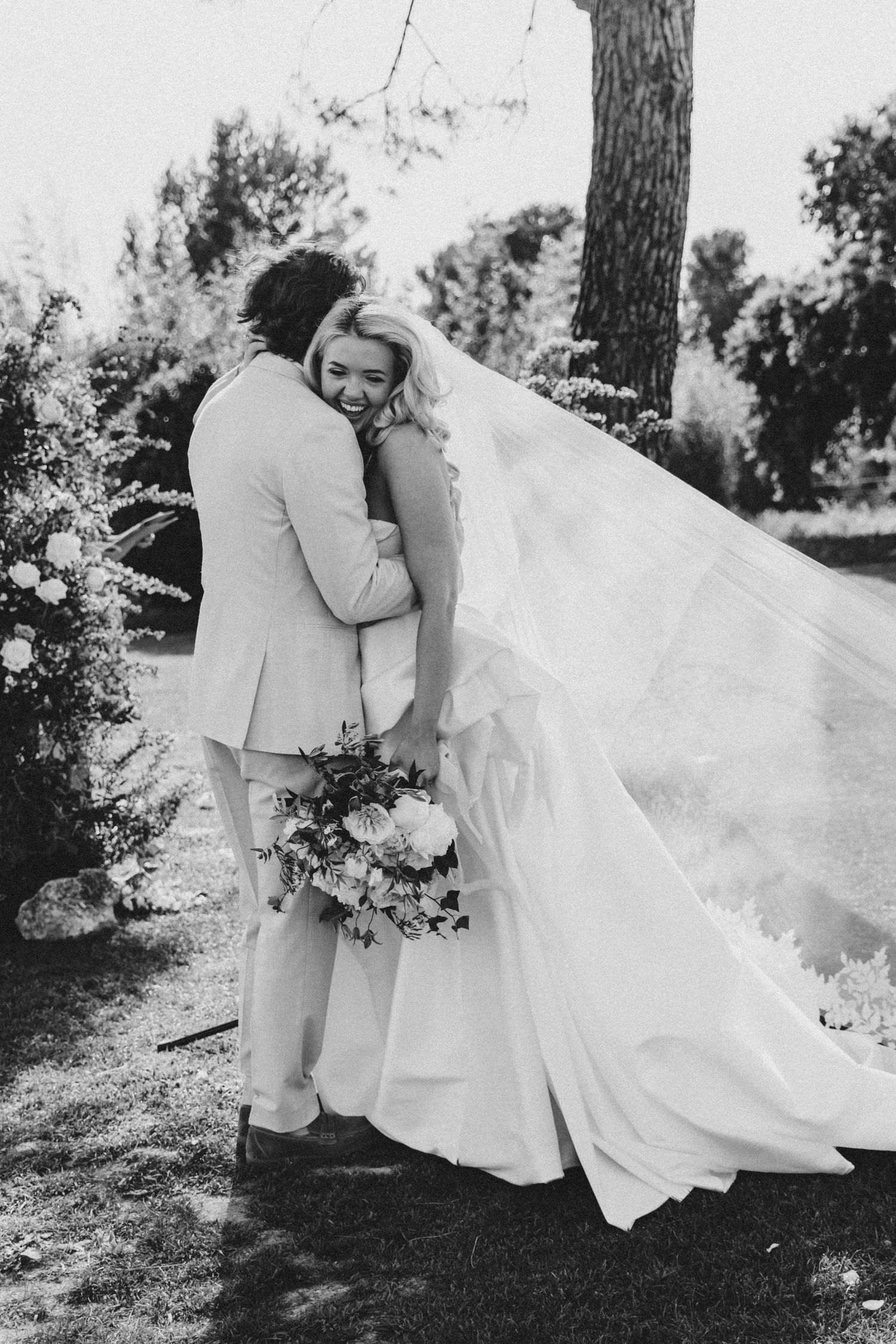 Black and white wedding photos showing romantic moments with flowing white dress and bouquet in outdoor setting.