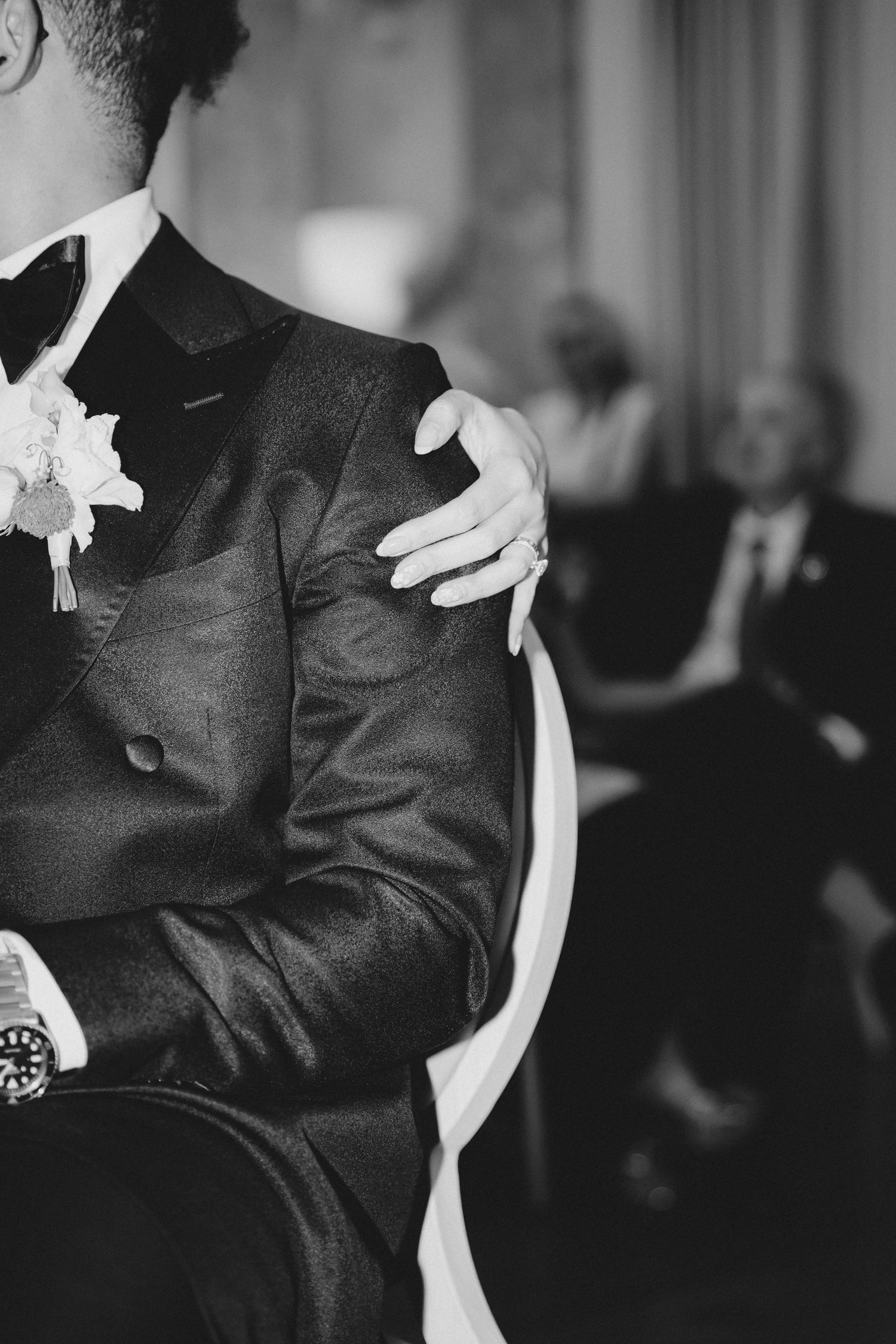 Black and white photo showing detail of groom's tuxedo with boutonniere and bow tie.