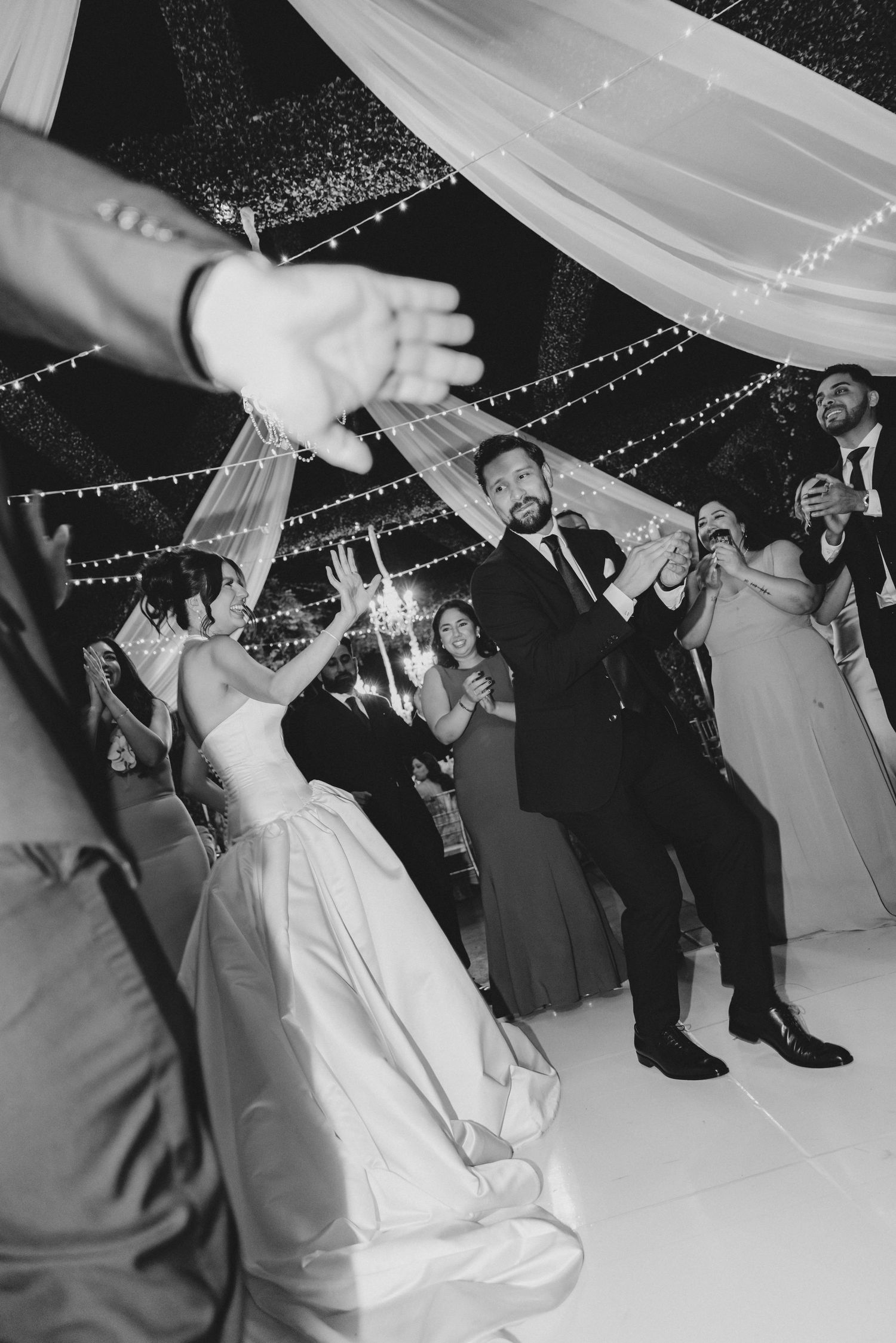 Wedding guests dance and celebrate under draped fabric and twinkling lights at an elegant black and white reception.