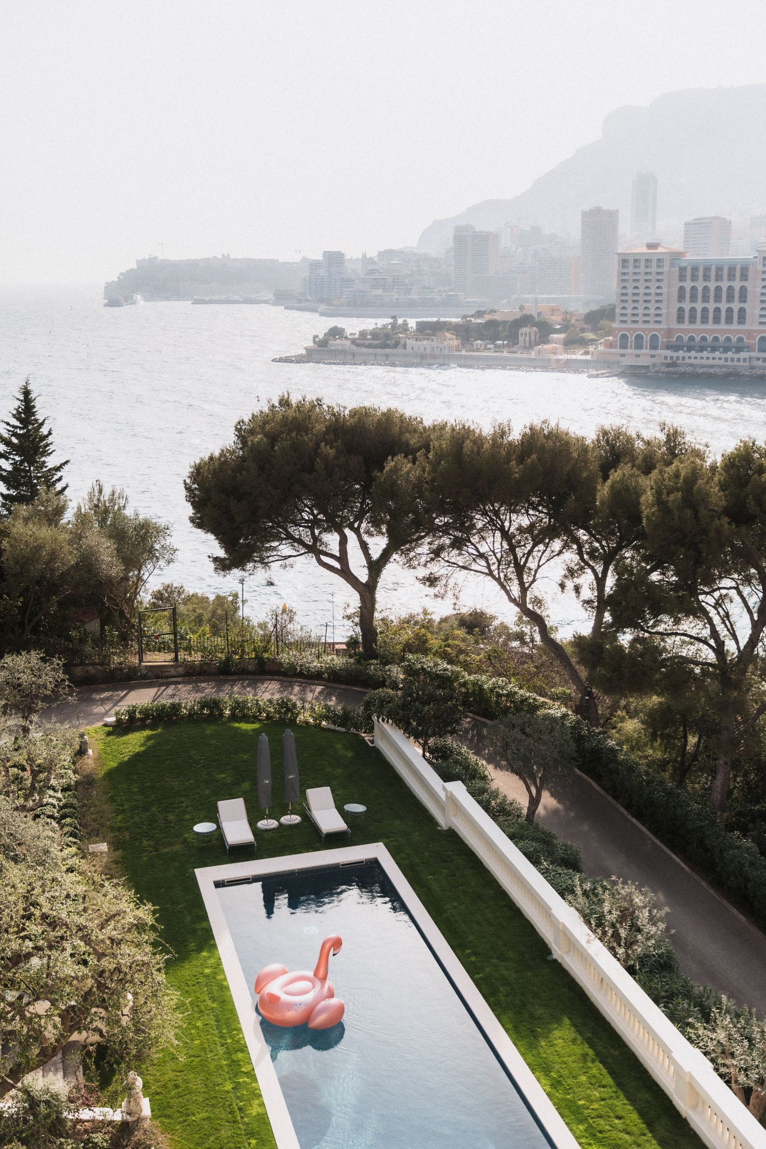 villa La Vigie - Luxury pool with pink flamingo float overlooking Monaco coastline and Mediterranean Sea surrounded by lush gardens.