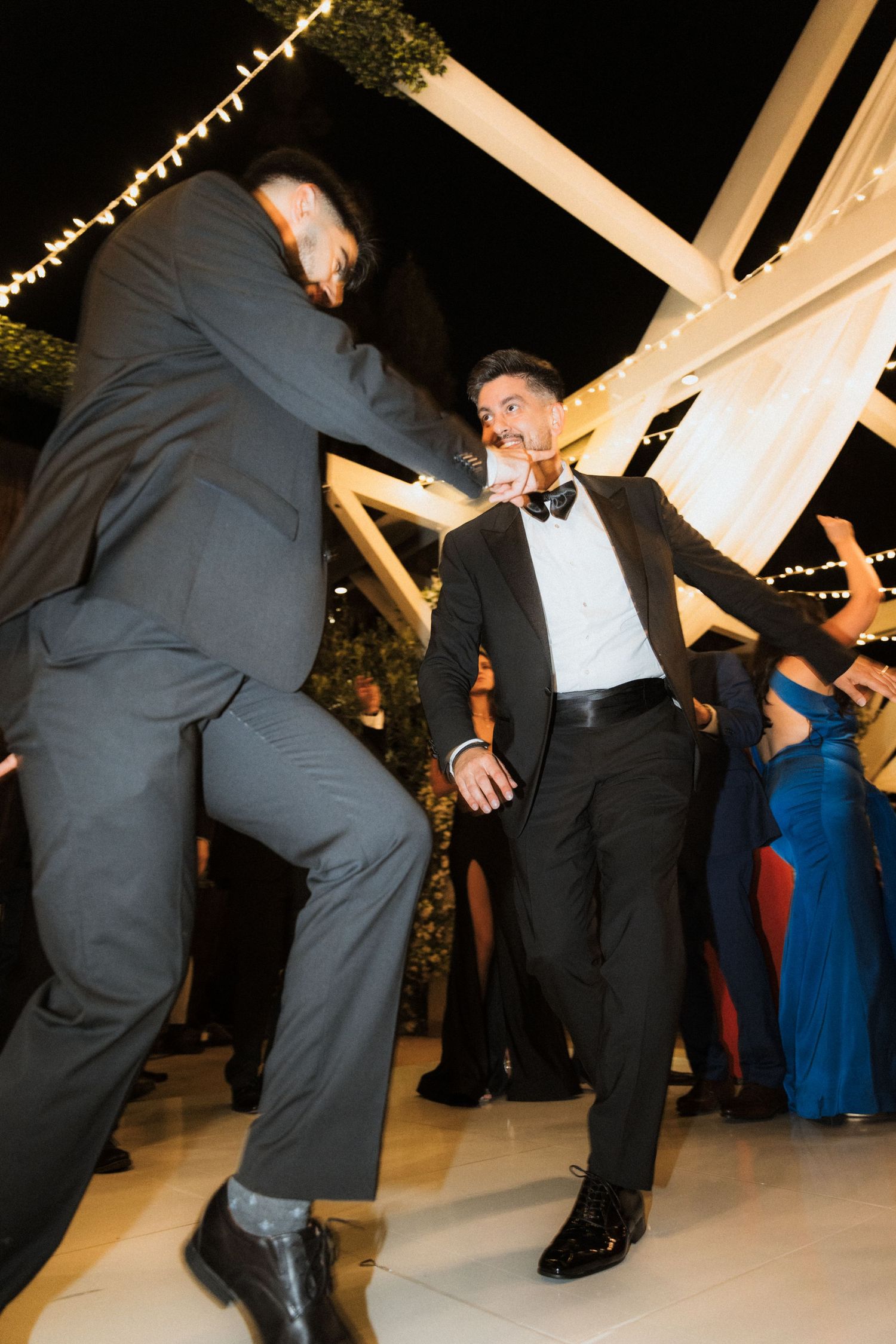 People dancing and having fun at a wedding reception with string lights visible overhead.
