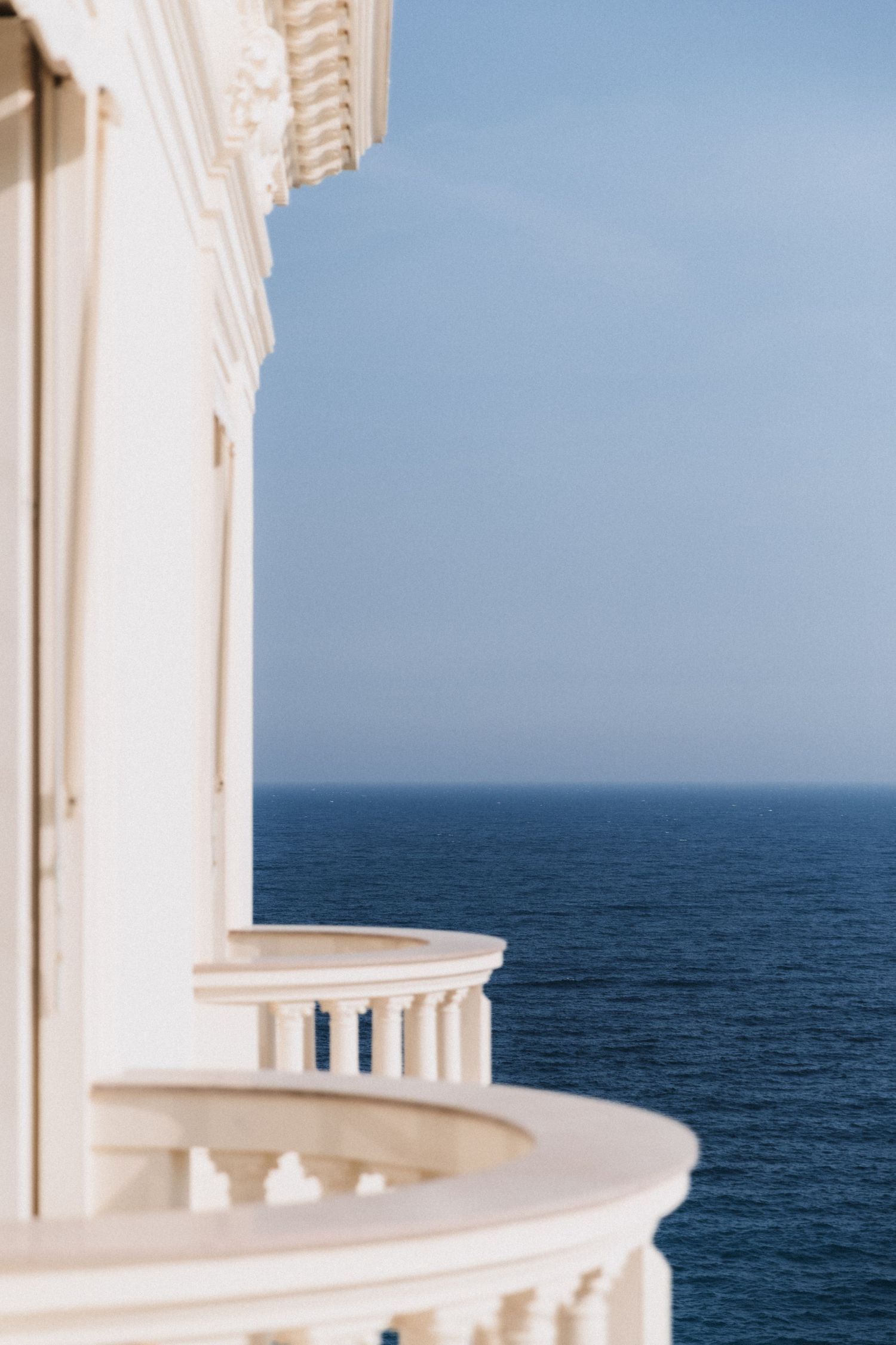 Villa La Vigie, Monaco - Elegant white curved balcony with ornate columns overlooking a deep blue ocean under a clear sky.