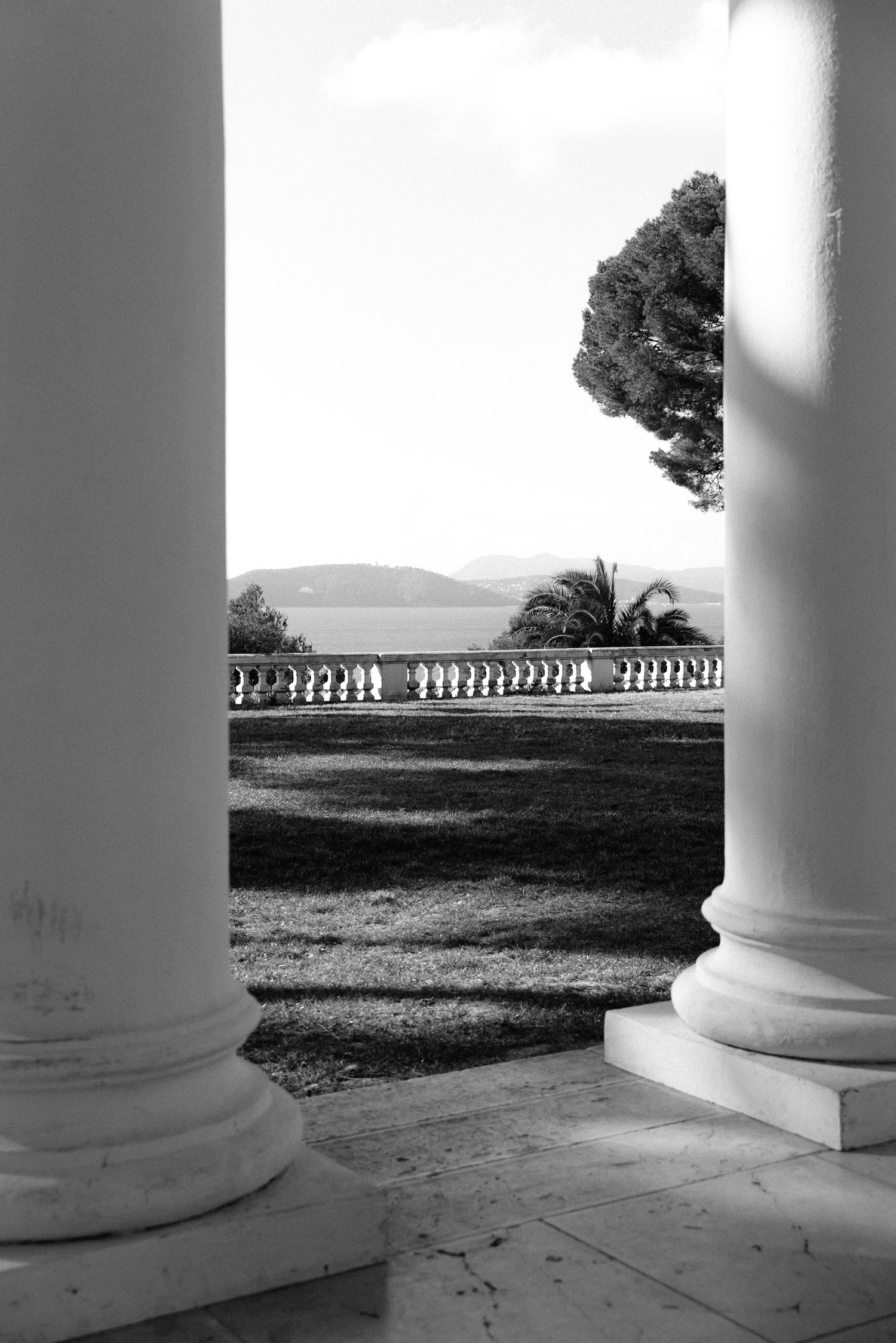 Villa Rocabella - Black and white photo of elegant columns framing a garden with balustrade, trees, and distant hills beyond.