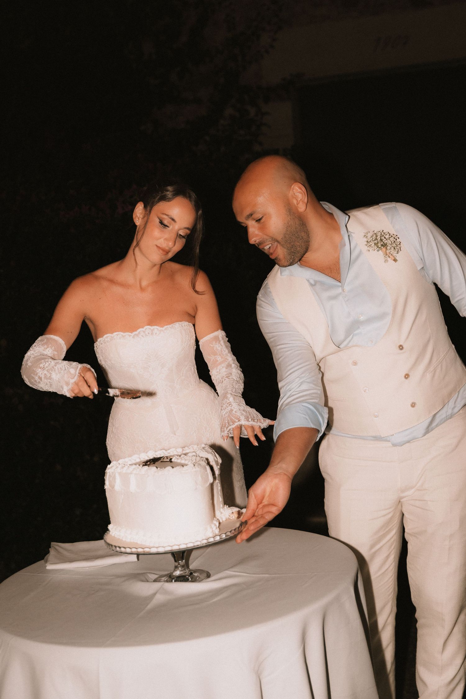 Couple in white attire cutting their wedding cake at the reception.