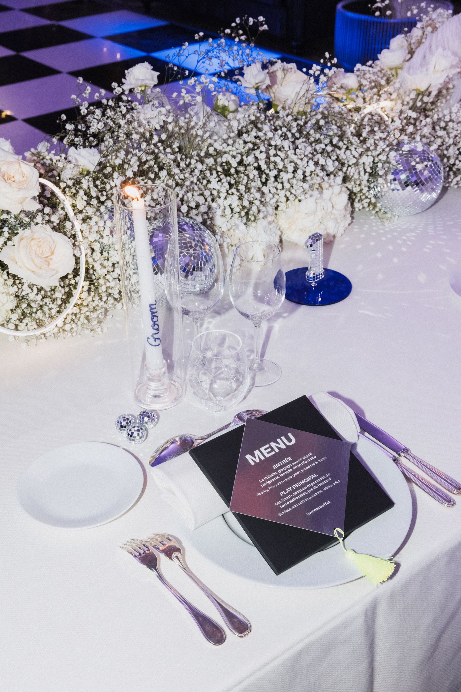 Wedding reception table setting with purple menu cards and white floral centerpieces.