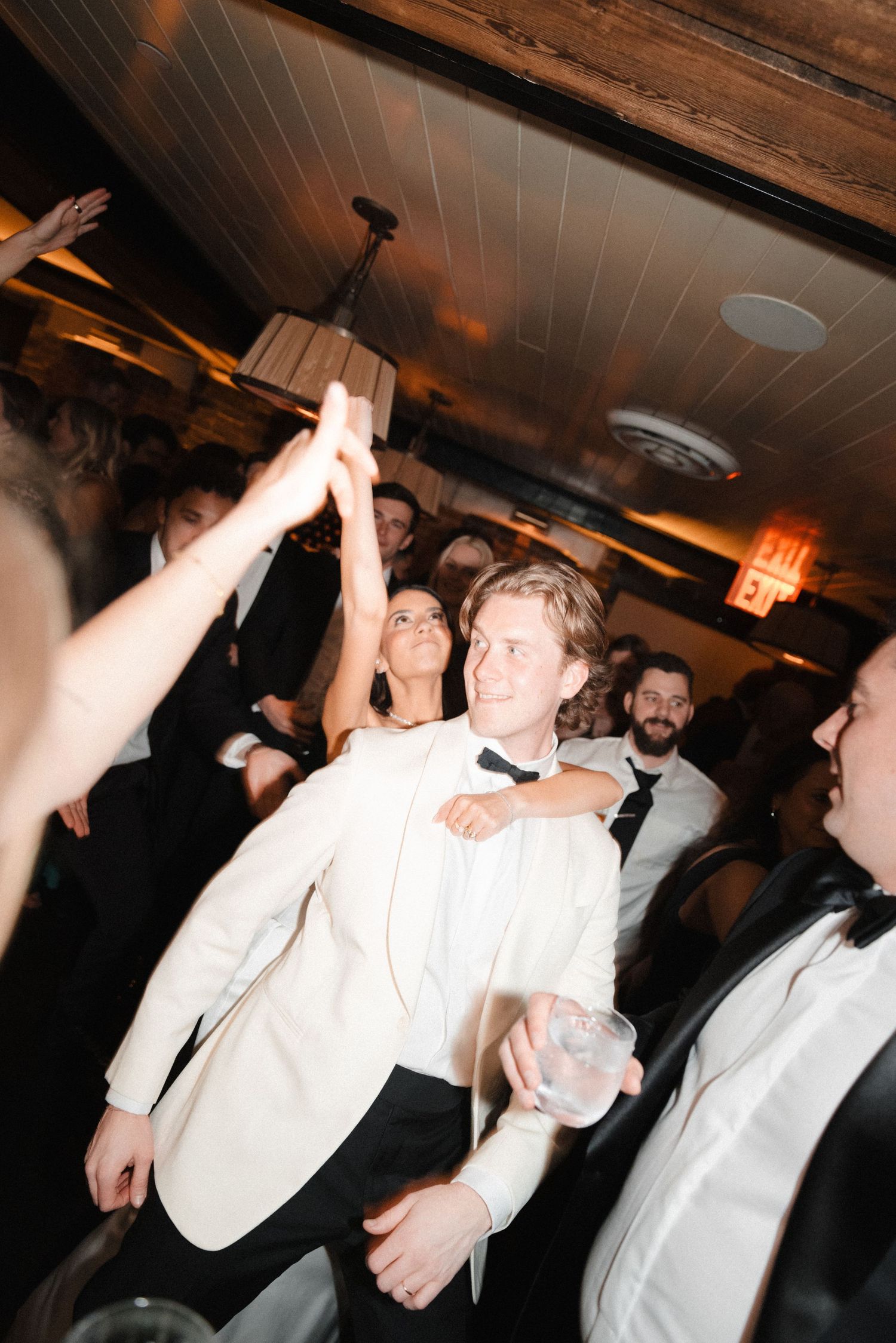 Groom in white tuxedo jacket celebrates on dance floor with guests at elegant wedding reception.