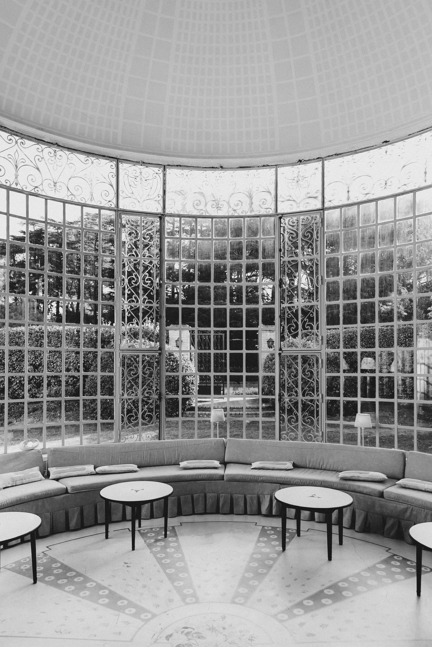Villa Rocabella - Black and white photo of an elegant circular room with curved sofa, ornate iron windows, and marble floor.