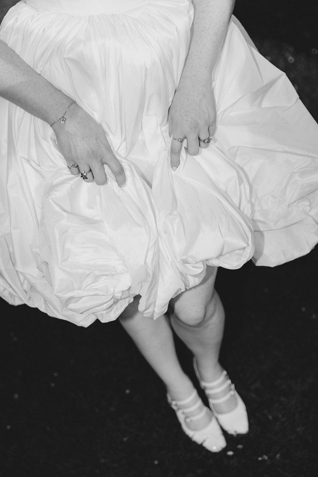 A black and white image showing white ballet shoes and flowing dress fabric against a dark background.