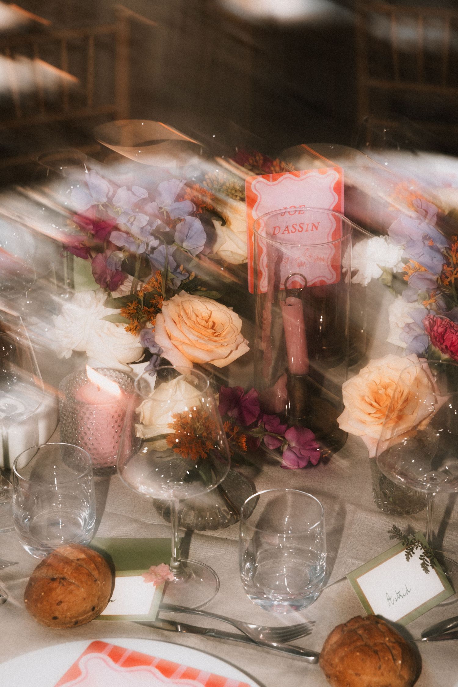 Romantic table setting with peach roses, wine glasses and candles in soft focus.