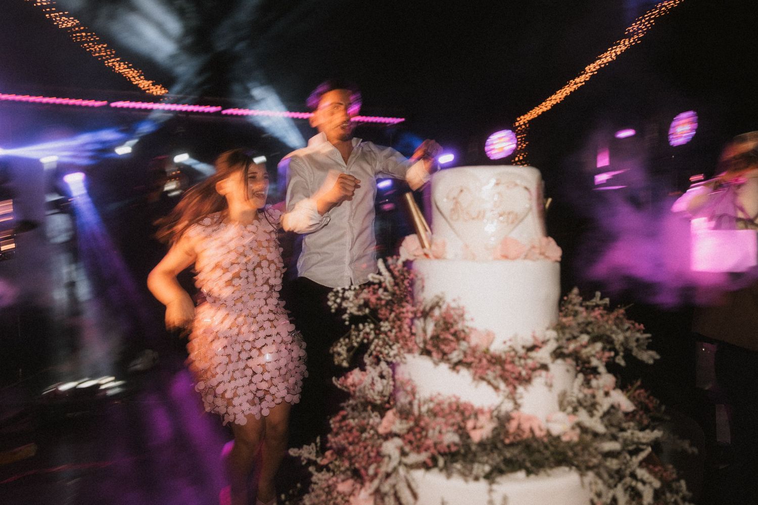 Couple dancing at wedding reception with disco lights and confetti in dark venue.