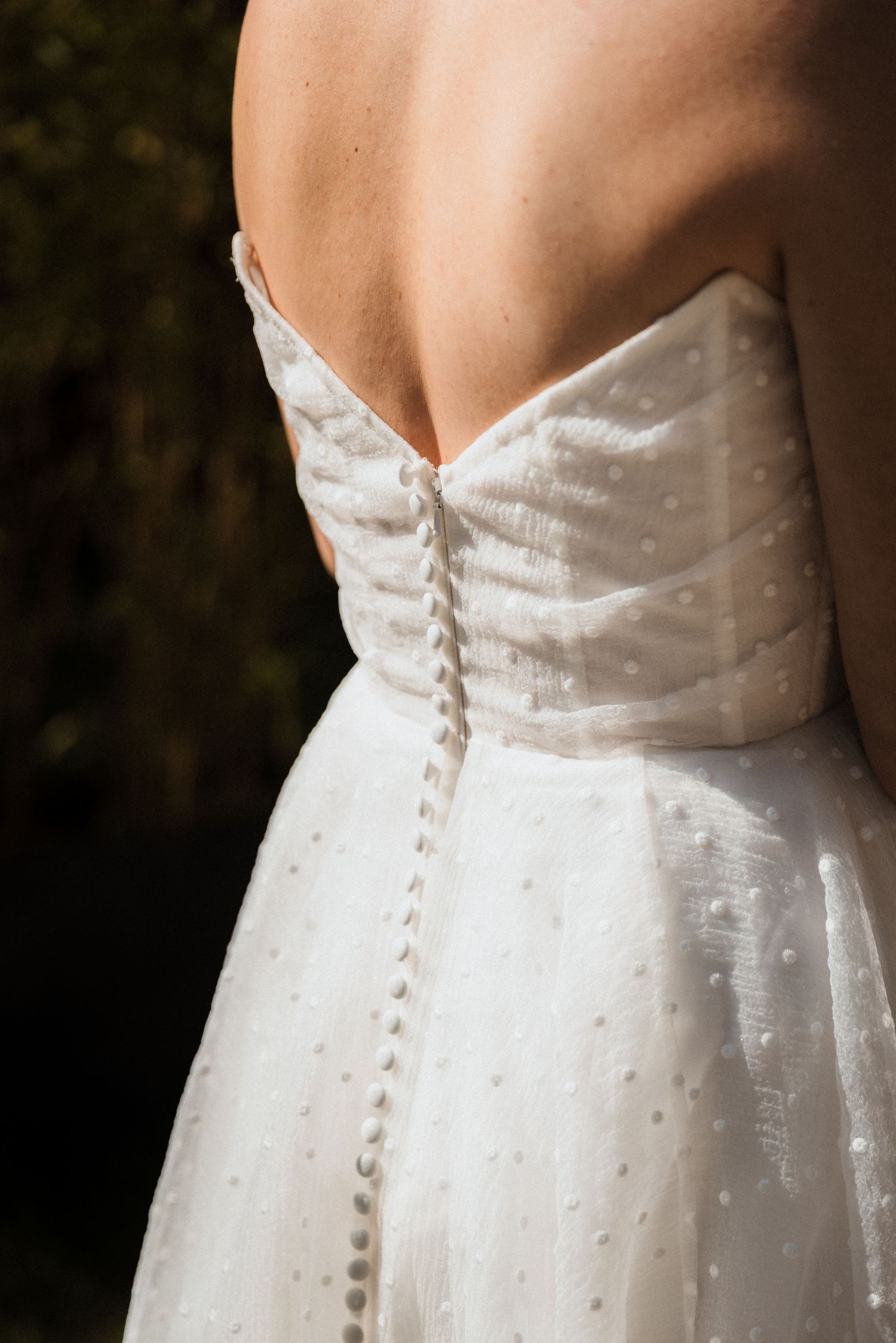 Close-up details of a white wedding dress with delicate button closures along the back.