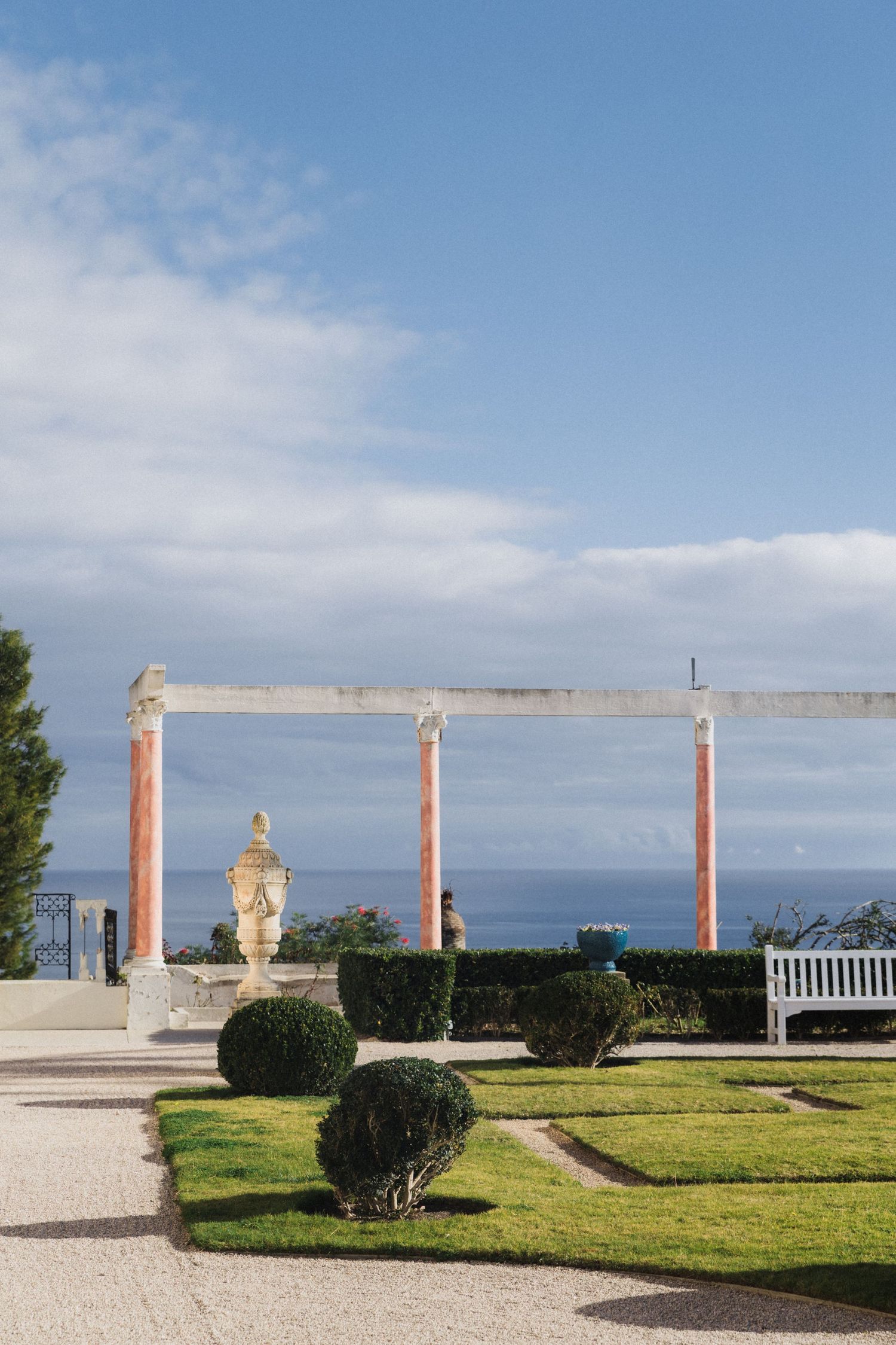 Villa Ephrussi de Rothschild - Elegant formal garden with red columns pergola, trimmed hedges, and stunning ocean view under blue sky.