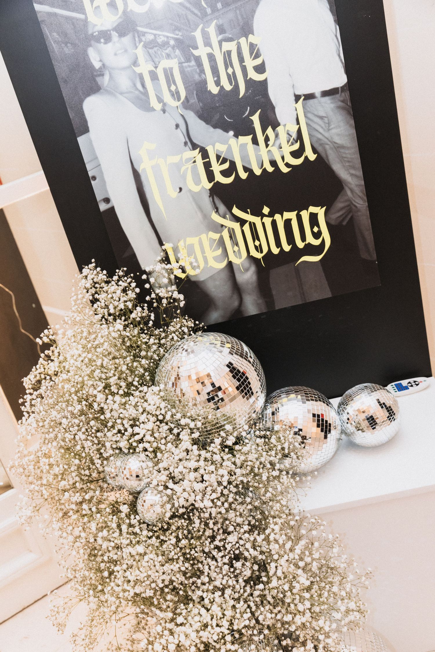 Wedding decor with baby's breath flowers, mini disco balls, and a black sign reading 'Welcome to the Fraenkel Wedding'.
