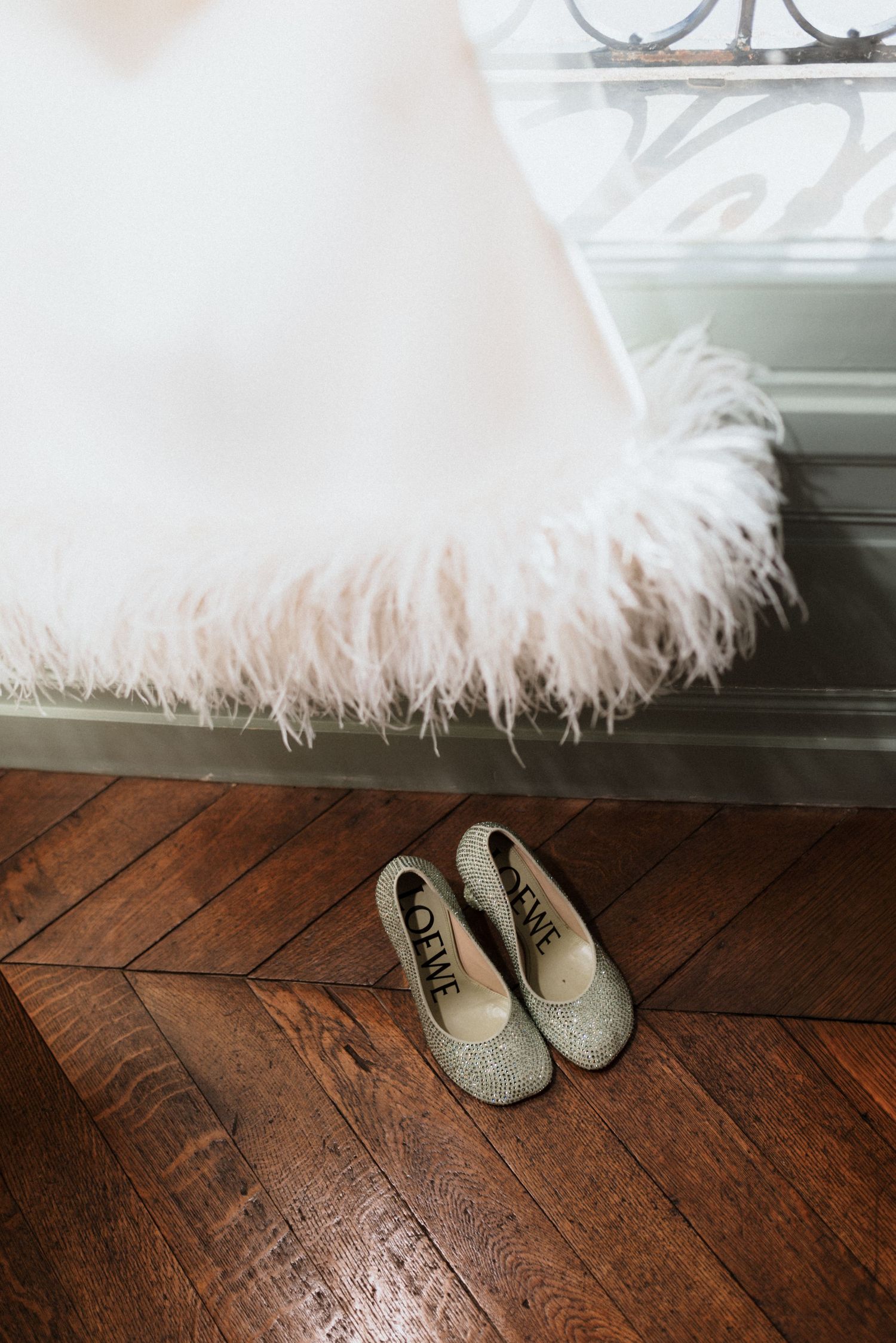 White feathered dress hem and silver ballet flats on a rustic wooden floor.